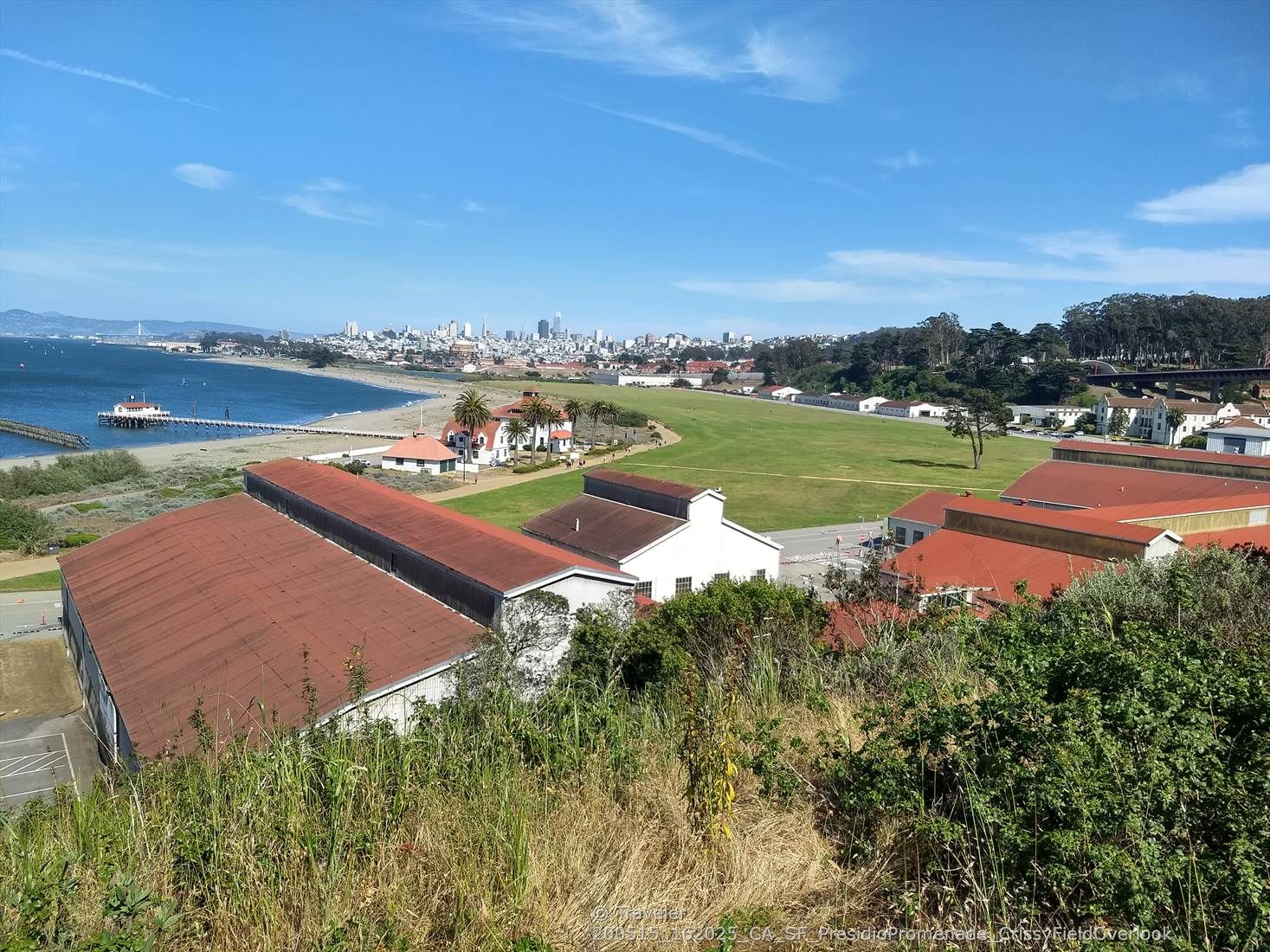 Coastal landscape with buildings, green field, beach, and distant city. Sunny. - San Francisco Bay Trail and Marin Headlands Loop