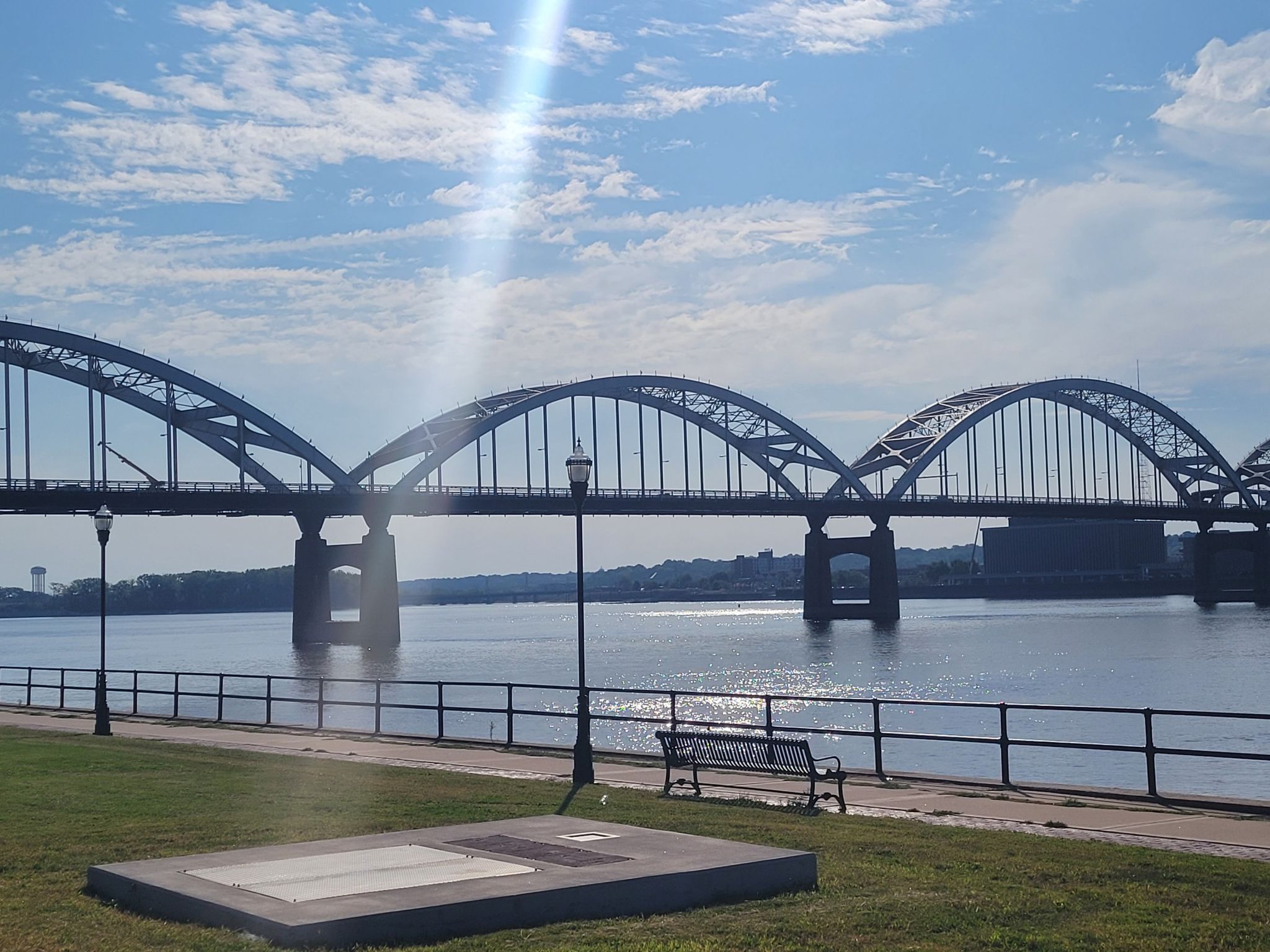 A large arched bridge over water, with a park bench and lamppost. - Schwiebert Riverfront Park – Sylvan Slough loop from Davenport