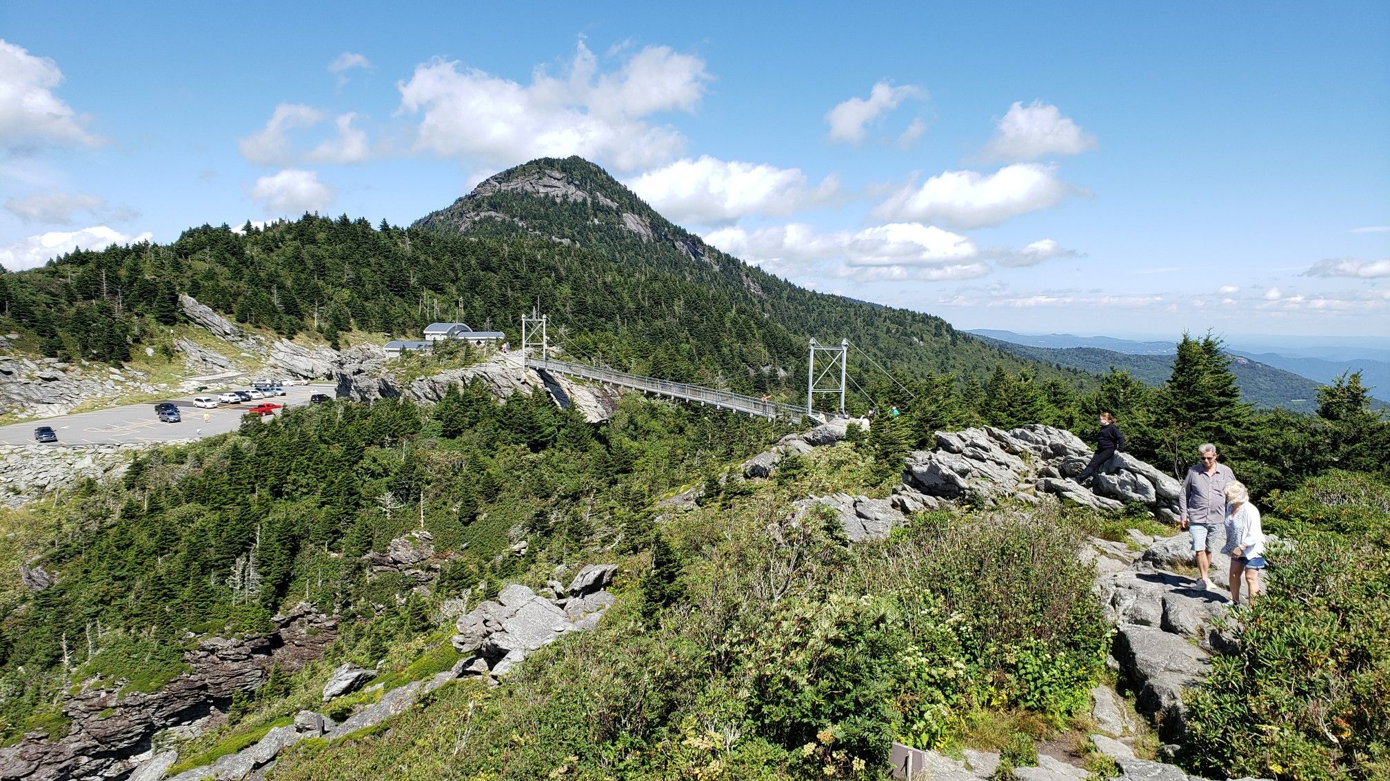 Mountain peak, suspension bridge, road, and hikers on a sunny day. - Grandfather and Underwood Trail Loop