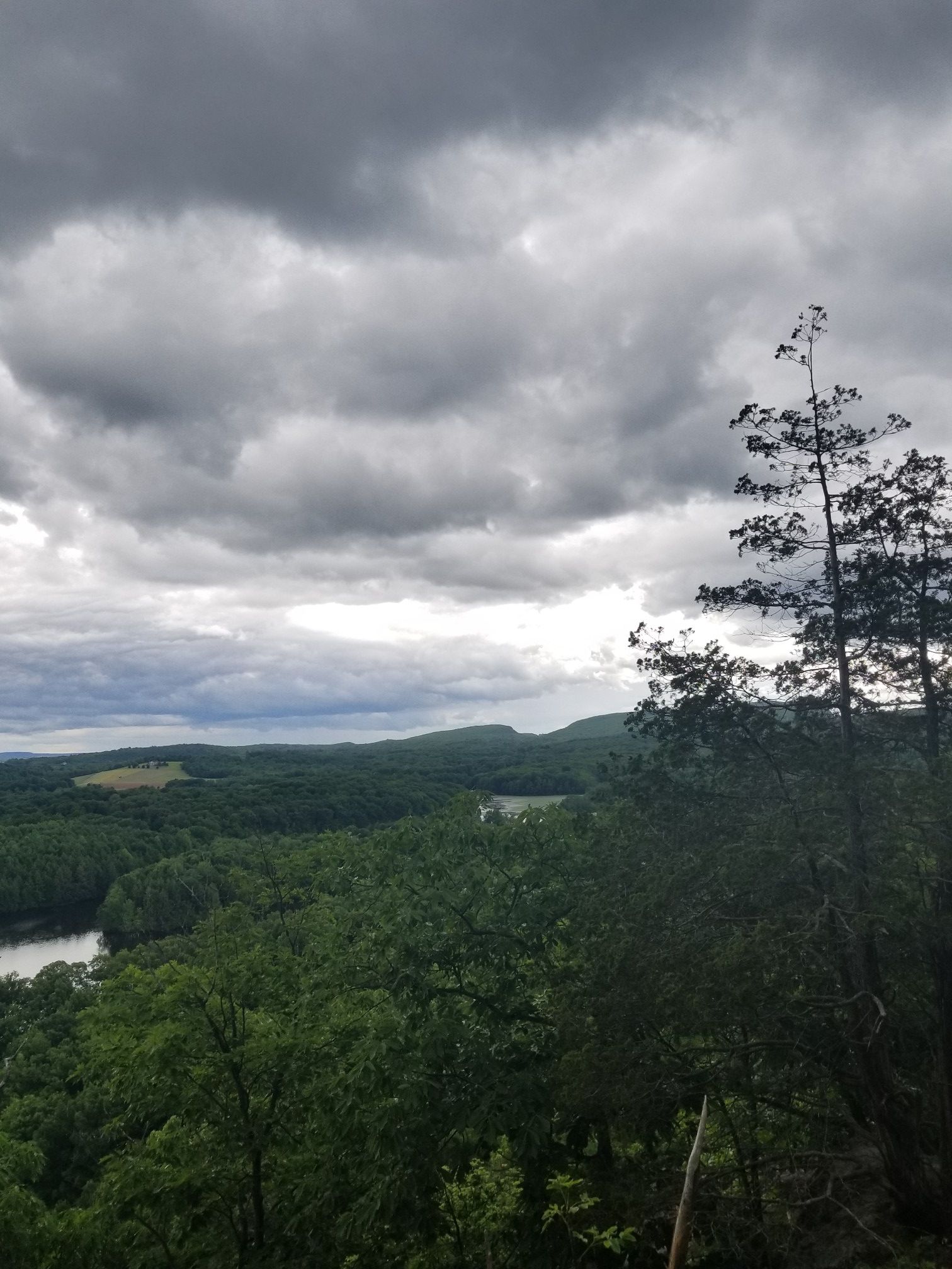 Dramatic cloudy sky over a vast green forest and distant lake. - Wassel Reservoir viewpoint – View of Lower Hart Pond loop from Ragged Mountain Memorial Preserve
