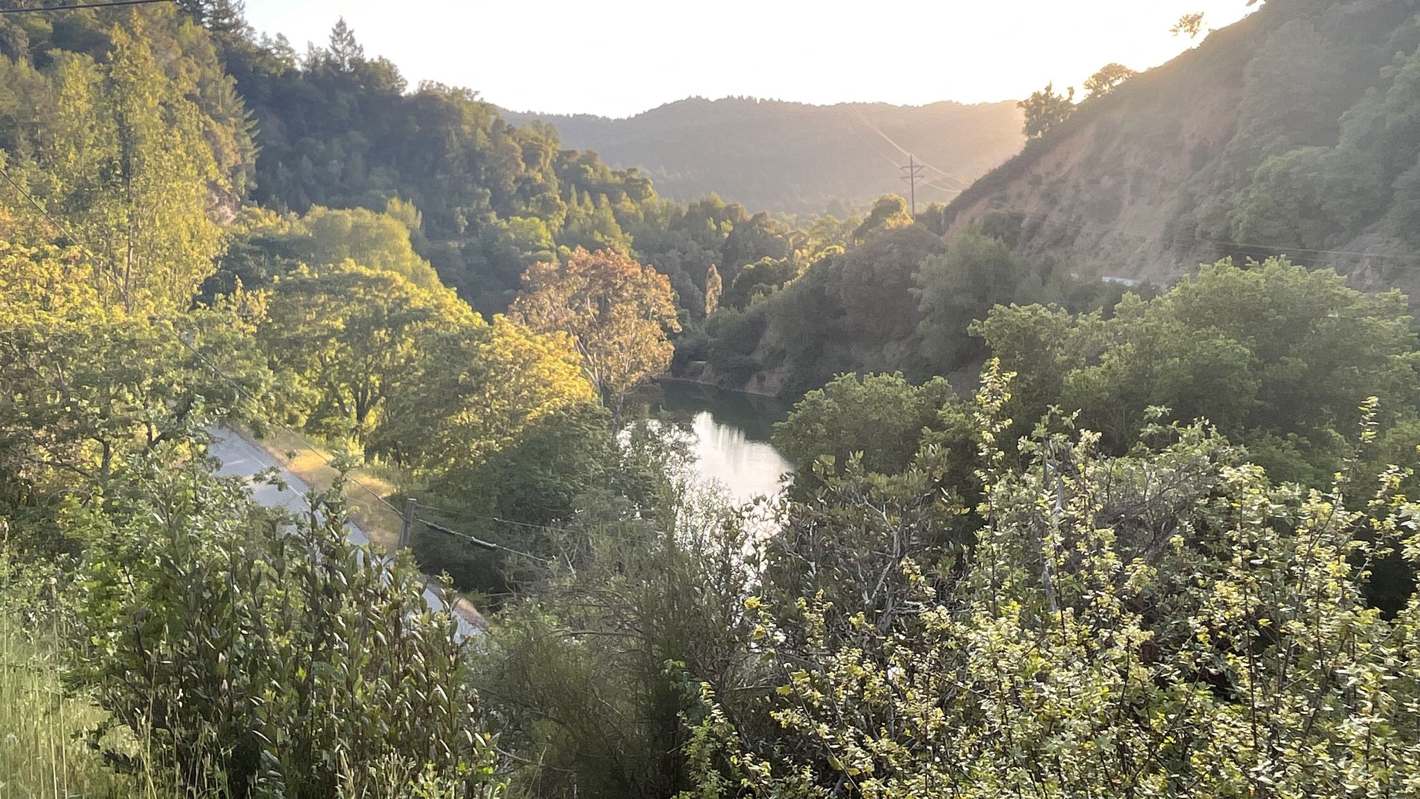 Sunlit river winding through a lush, green forested valley. - Soda Springs Road