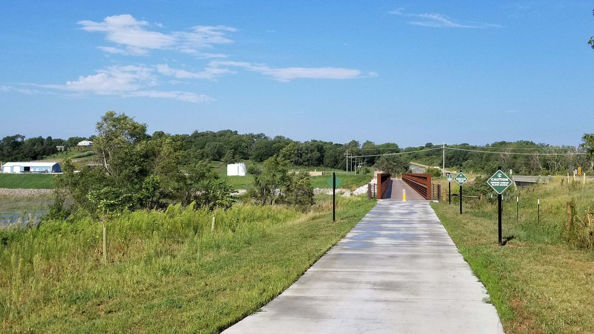 Paved path leading to a bridge over water, surrounded by green landscape. - Glenn Cunningham Lake – Cunningham Lake Bridge loop from Glenn Cunningham Lake Park