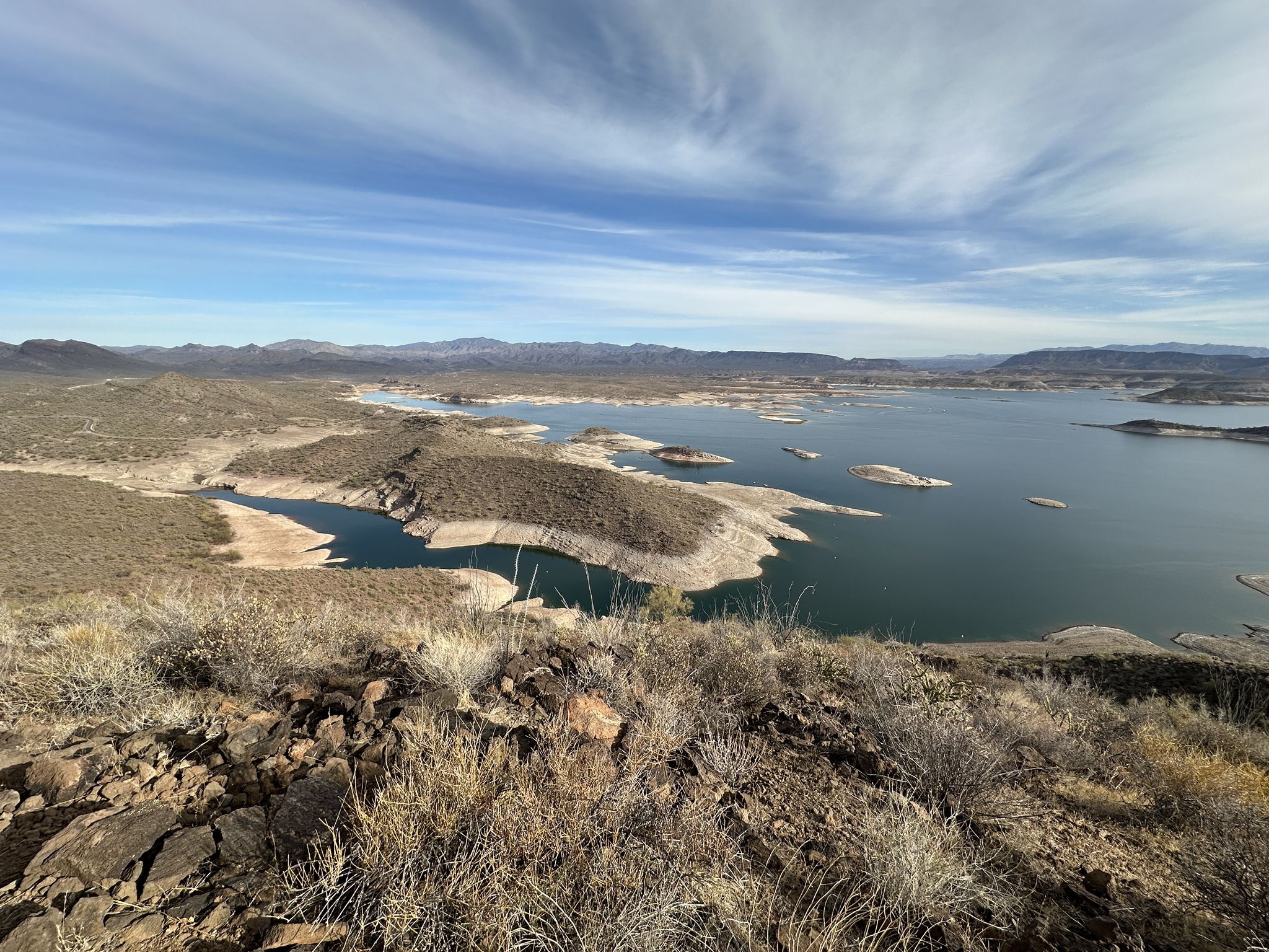 Expansive desert lake with islands, surrounded by arid hills under a cloudy sky. - Pipeline Canyon Trail