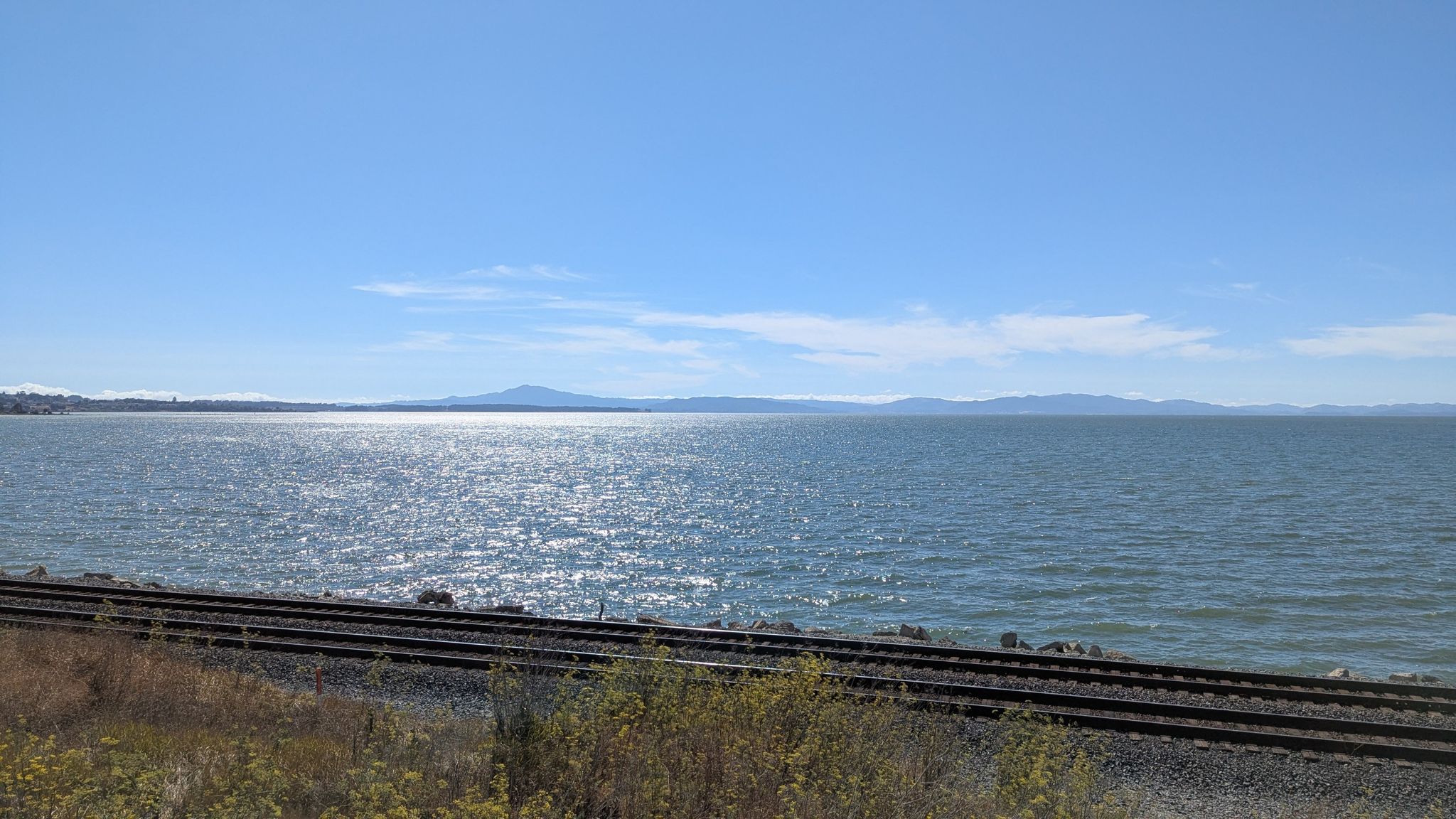Sunlit water with train tracks in the foreground and distant mountains under a clear sky. - Lone Tree Point Regional Park loop from Hercules