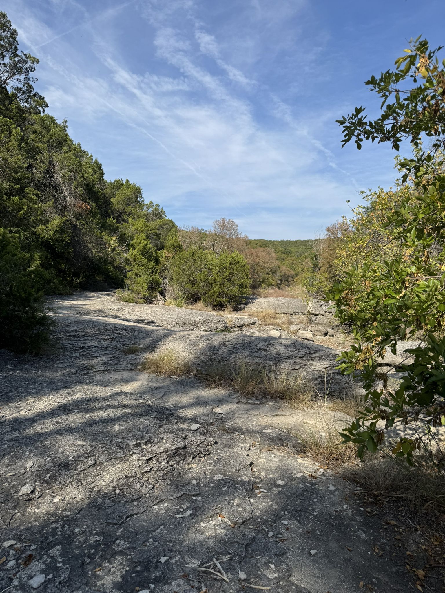 A wide, rocky riverbed under a bright blue sky with scattered clouds. - Violet Crown Trail: Zilker Trailhead to 360 Trailhead