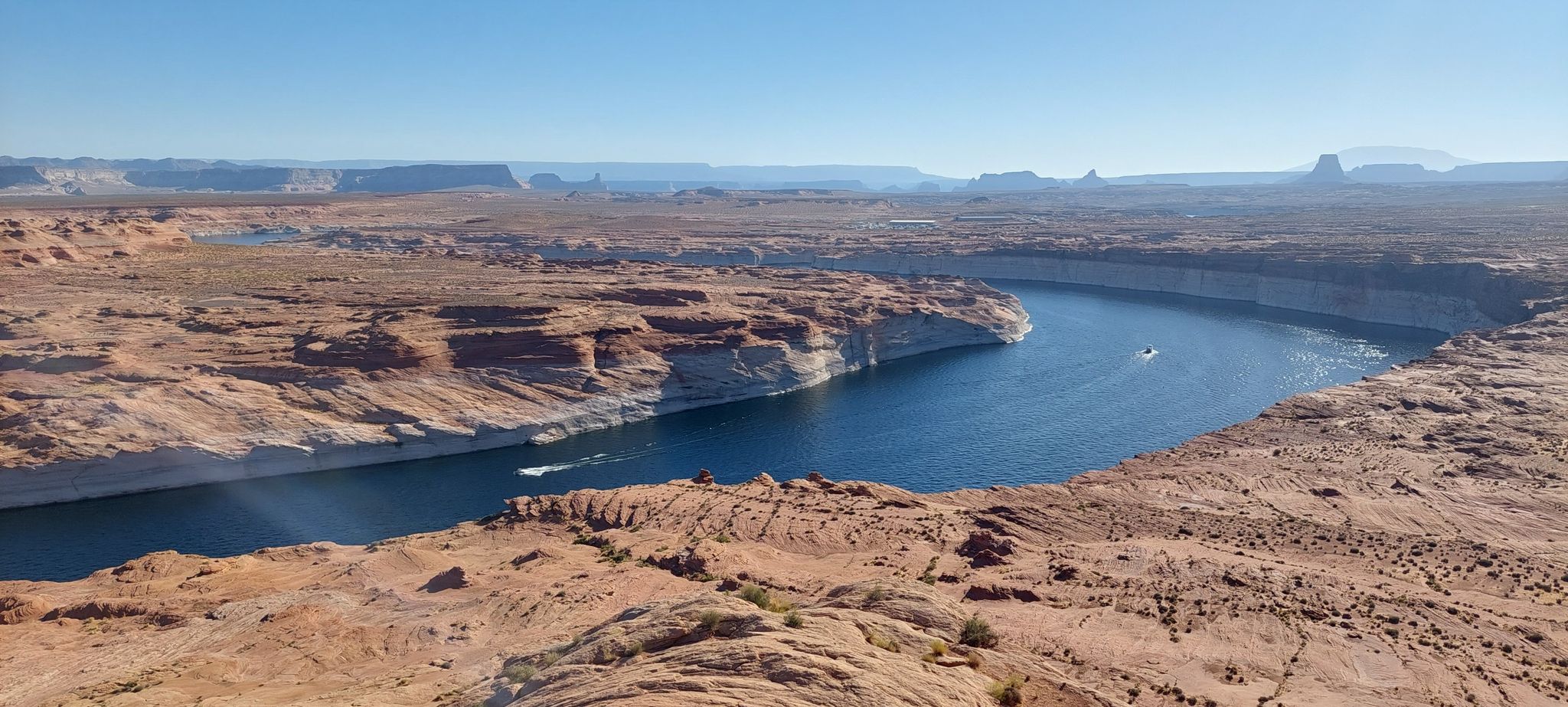 Blue river winds through red rock canyons, two boats on the water. - Rimview Trail