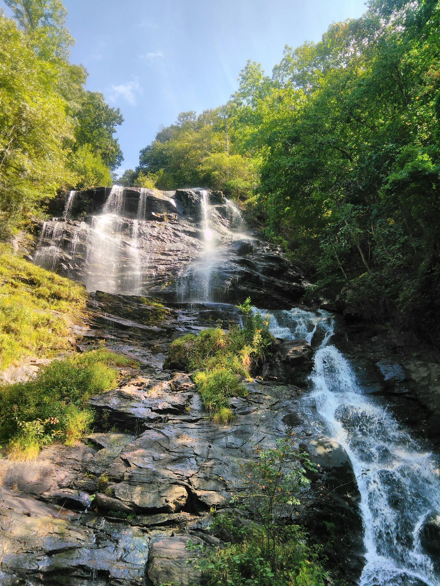 A tall, multi-tiered waterfall cascades down a rocky, green hillside. - Mountain Laurel and Creek Trail Loop