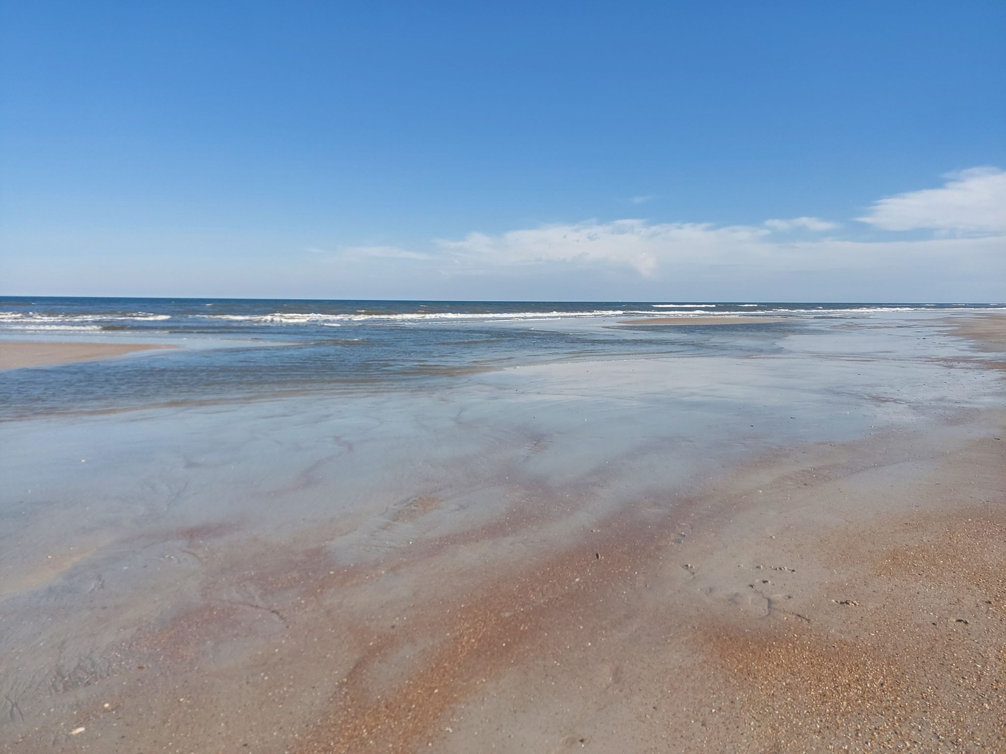 Expansive wet sandy beach reflecting blue sky, with gentle waves. - Bike loop from Saint Augustine Beach