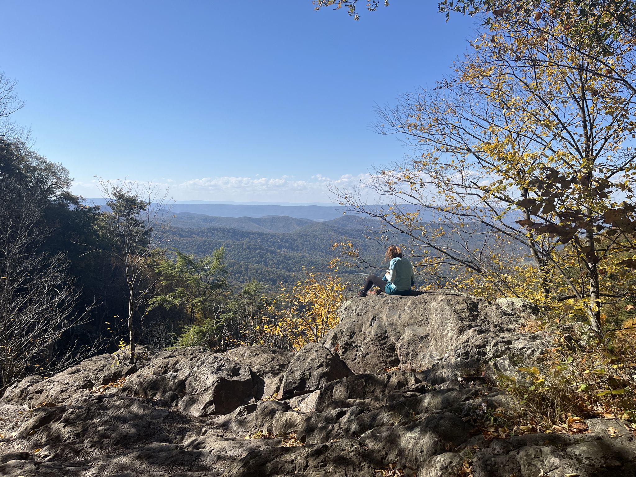 A person sits on a rock overlooking a vast mountain landscape. - Lewis Falls loop from Big Meadows Wayside