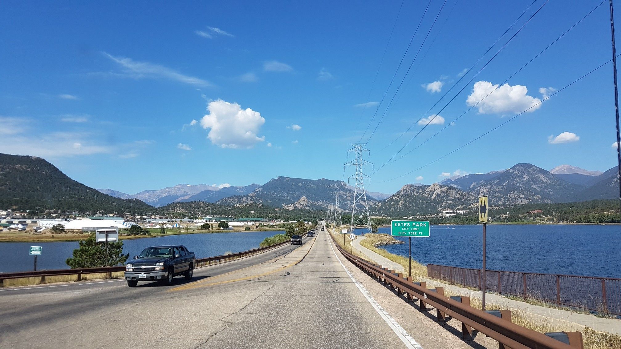 Road bridge over a lake, with cars, mountains, and a bright blue sky. - Lake Estes – Limber Pine Trail loop from Fish Creek