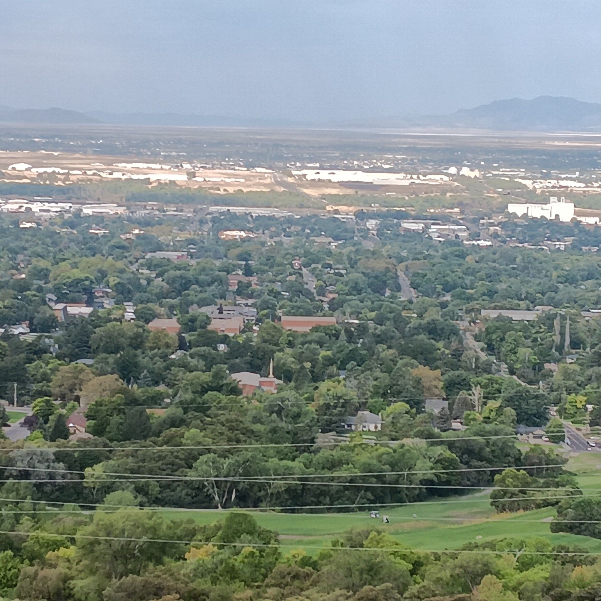 Expansive hazy view of a green, tree-filled town with distant mountains. - Waterfall Canyon Trail