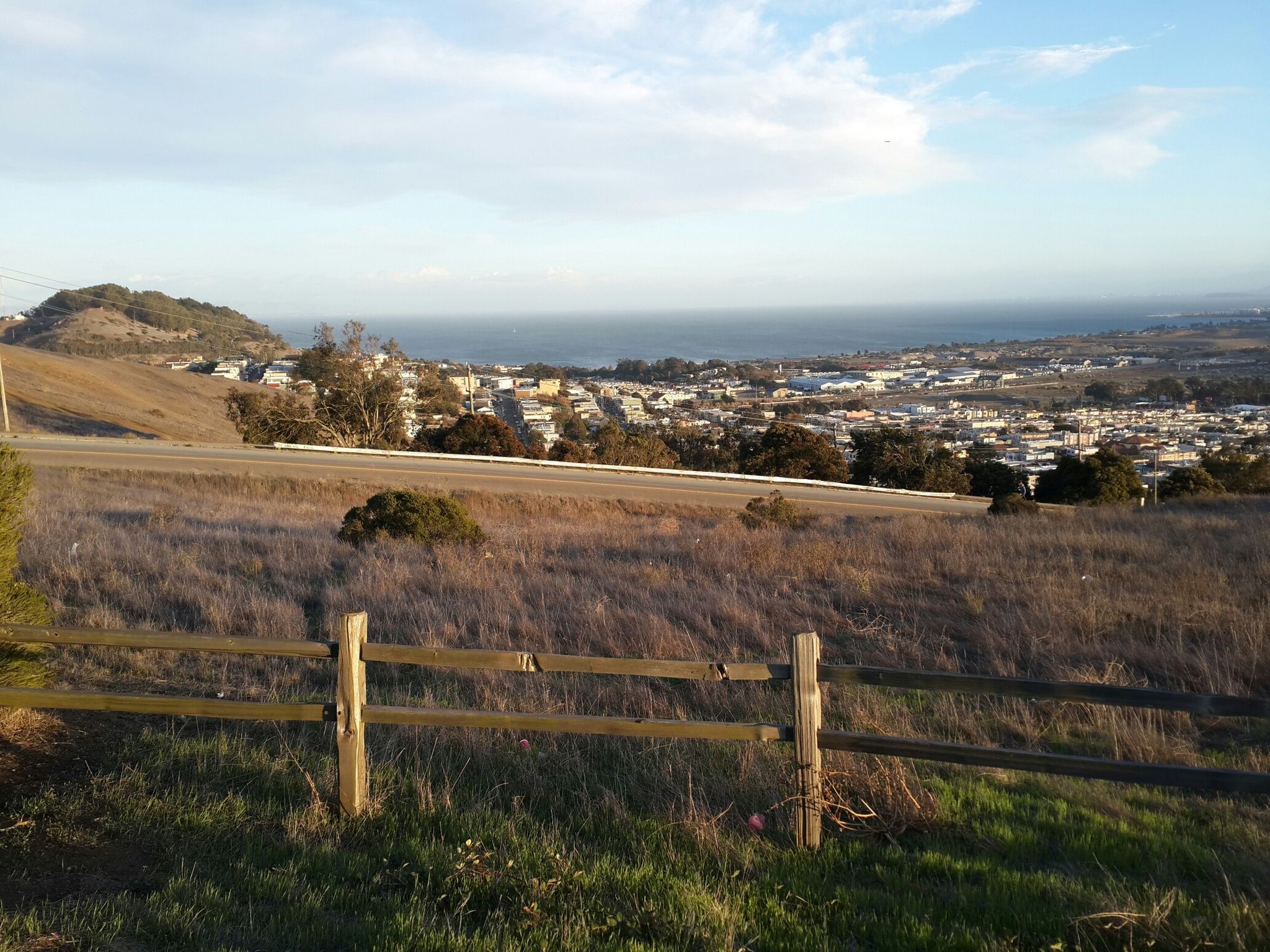 Wooden fence in a grassy field overlooking a city and ocean at sunset. - Philosopher's Way