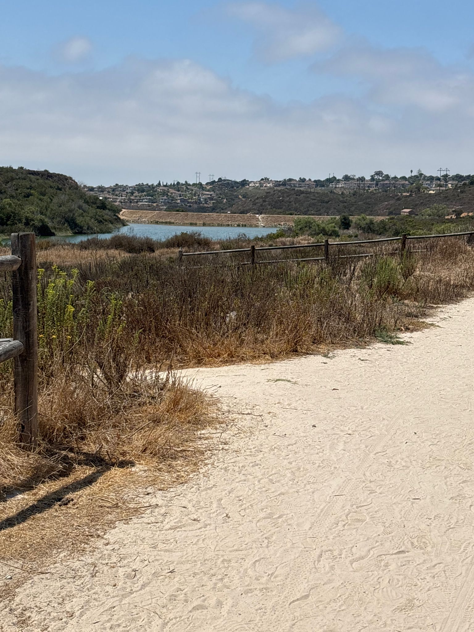 A dirt path next to a fence, overlooking a distant lake and hills. - Lake Calavera Loop Trail
