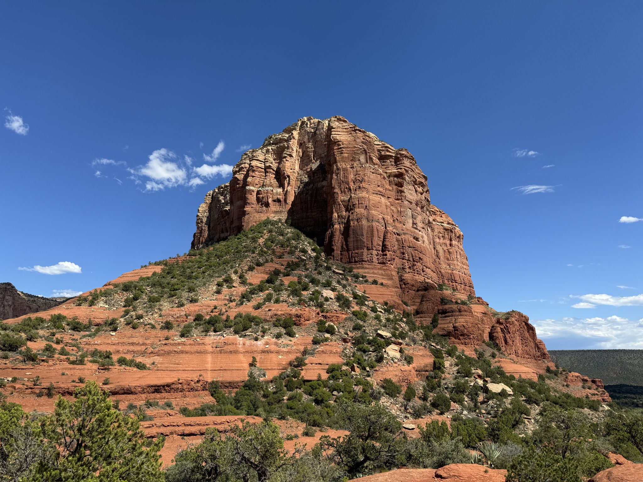 Large red rock mountain covered in green shrubs under a bright blue sky. - Courthouse Butte and Bell Rock Loop Trail