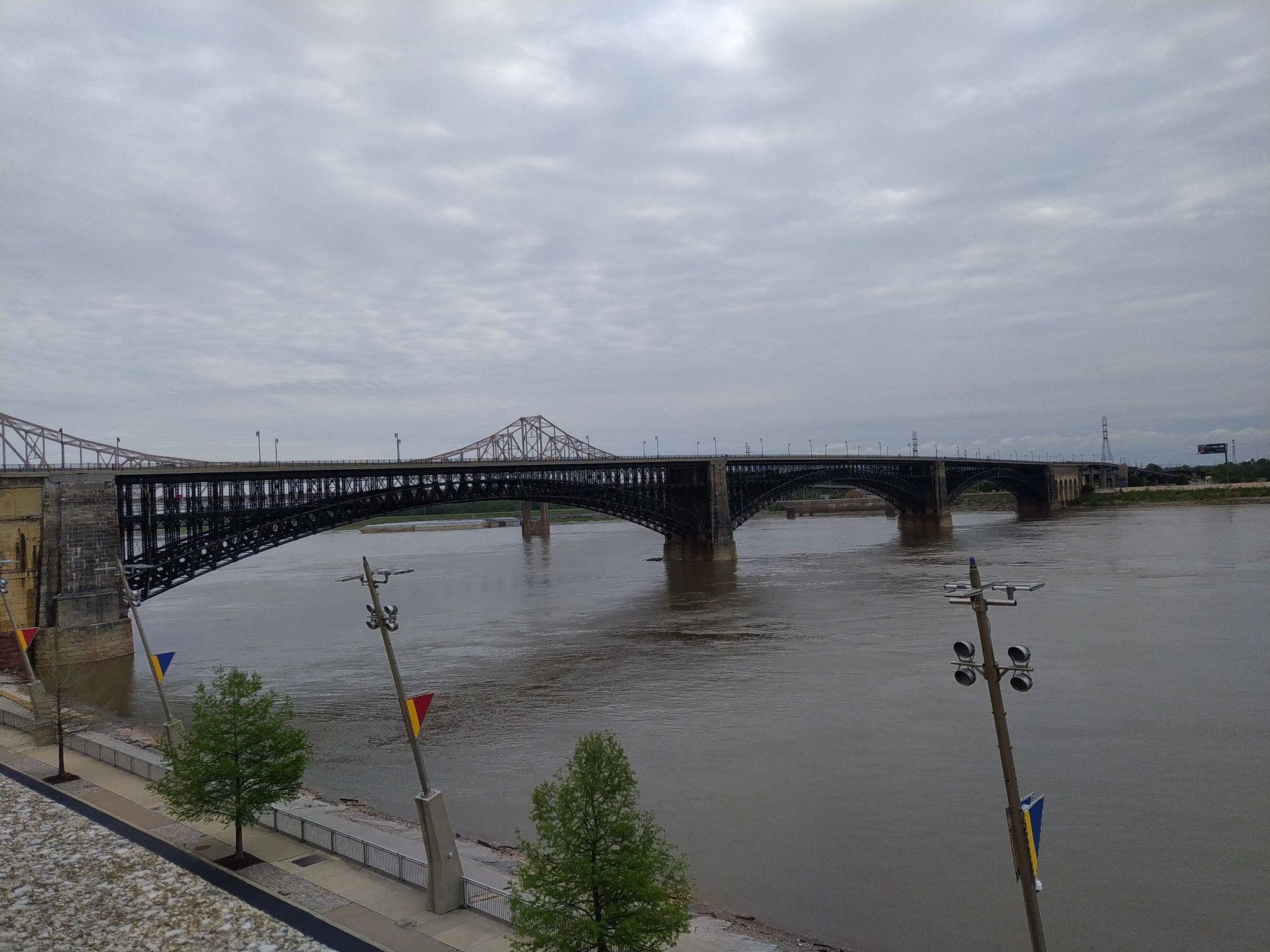 A long metal bridge crosses a wide river under an overcast sky. - Luther Ely Smith Square – Eads Bridge loop from St. Louis
