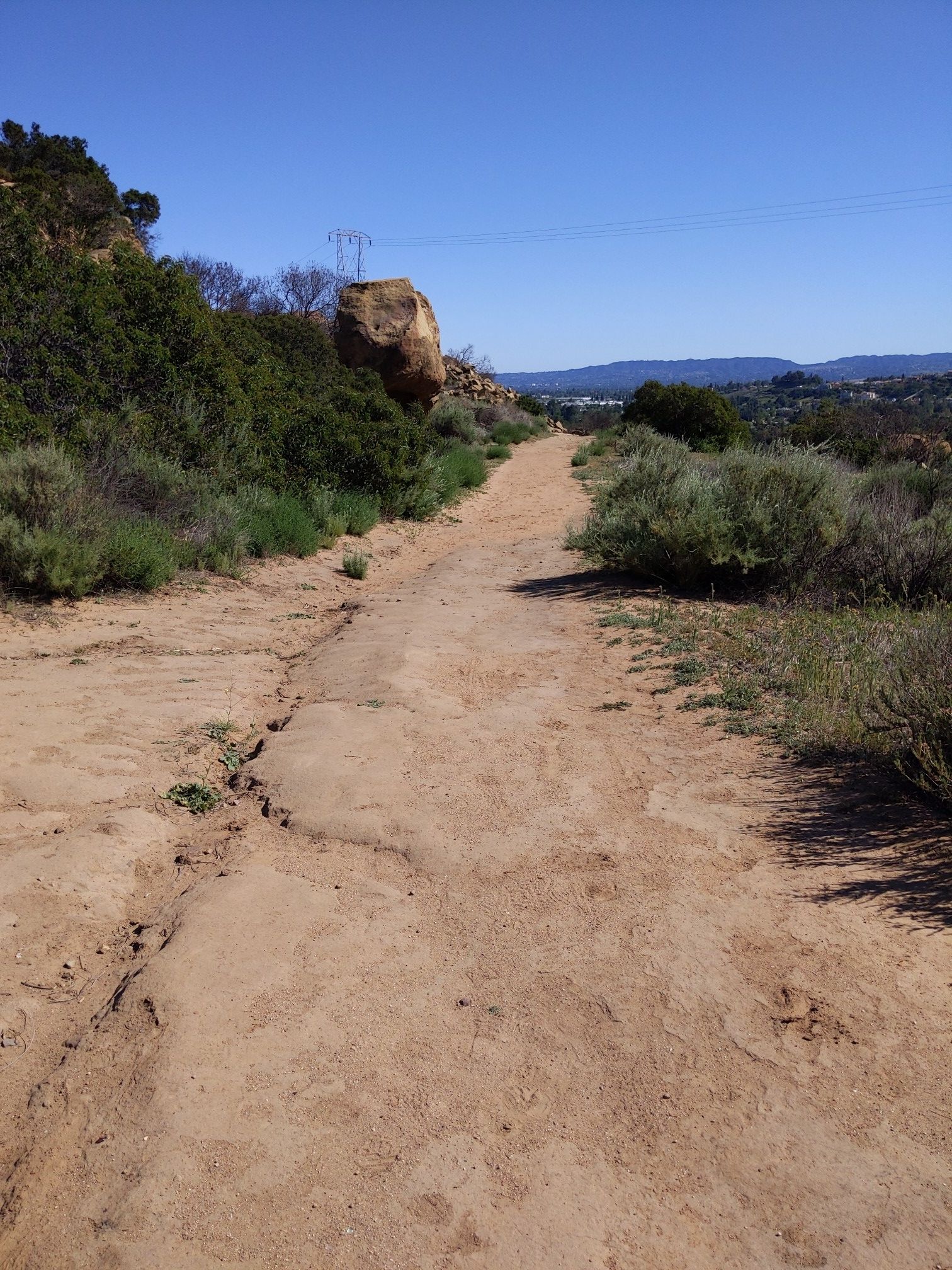 A sunny dirt path winds through arid scrubland with distant hills. - Old Santa Susanna Stagecoach and Mattingly Trail Loop