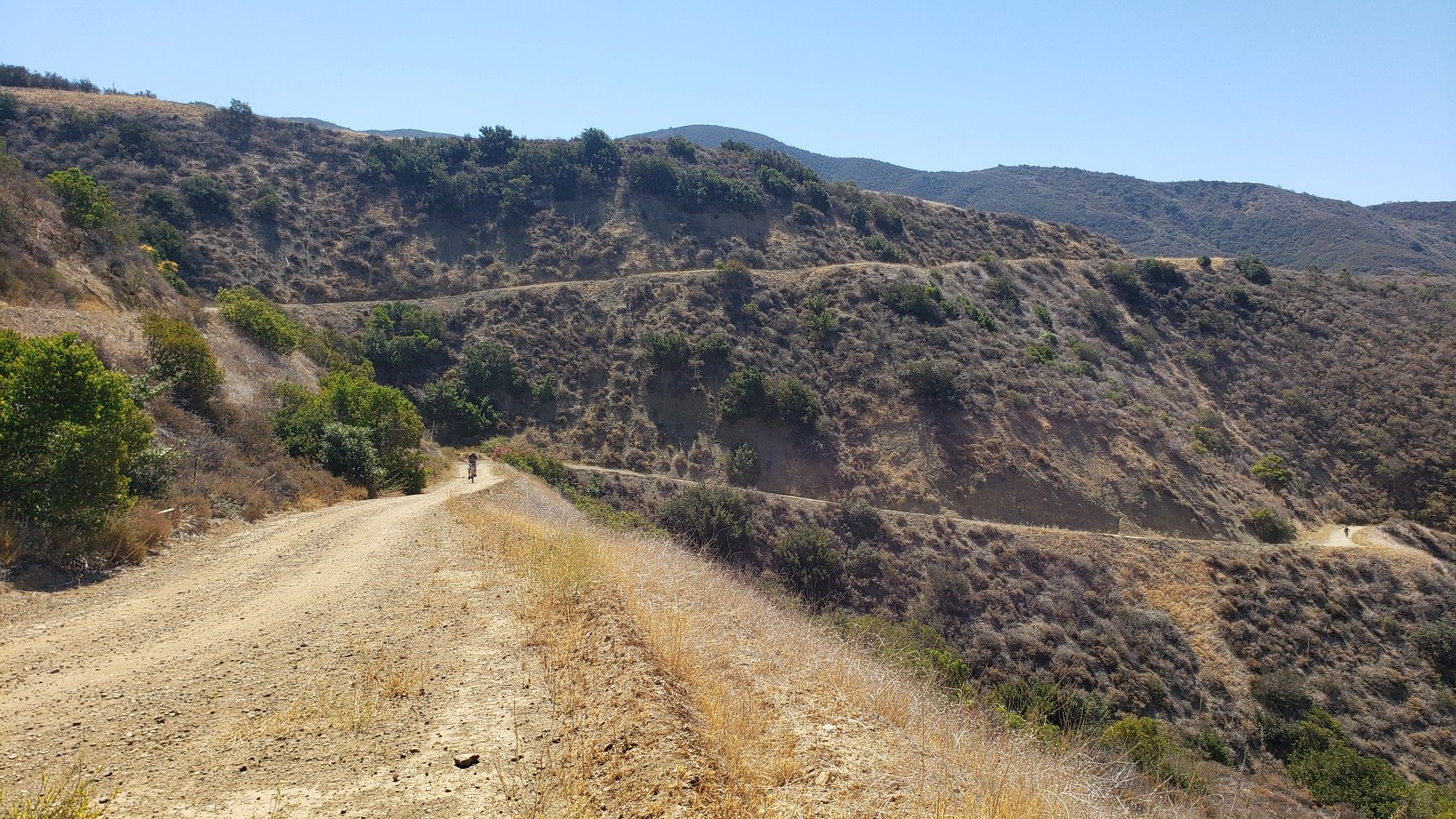 A person walks on a winding dirt road across dry, scrubby hillsides. - Black Star Falls – Black Star Canyon Road loop from Black Star Canyon