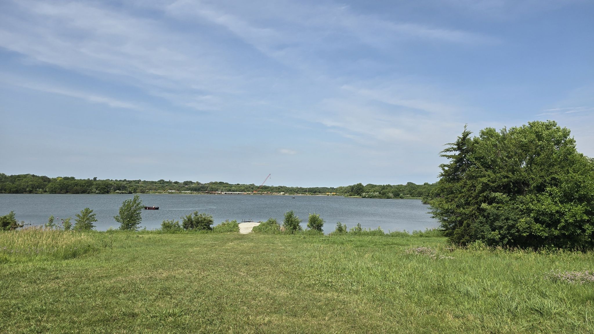 Sunny view of a lake with green grassy foreground and distant trees. - West Papio Creek Bridge – Zorinsky Dam loop from Douglas