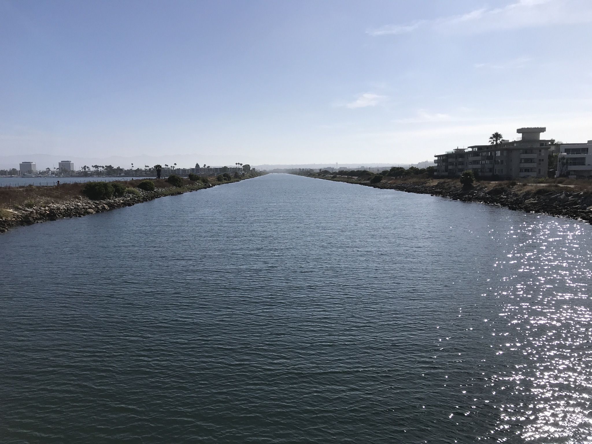 A wide canal with calm water, distant buildings, and bright sunlight reflecting. - Manhattan Beach – El Segundo Beach loop from Catalina Avenue / Elena Avenue