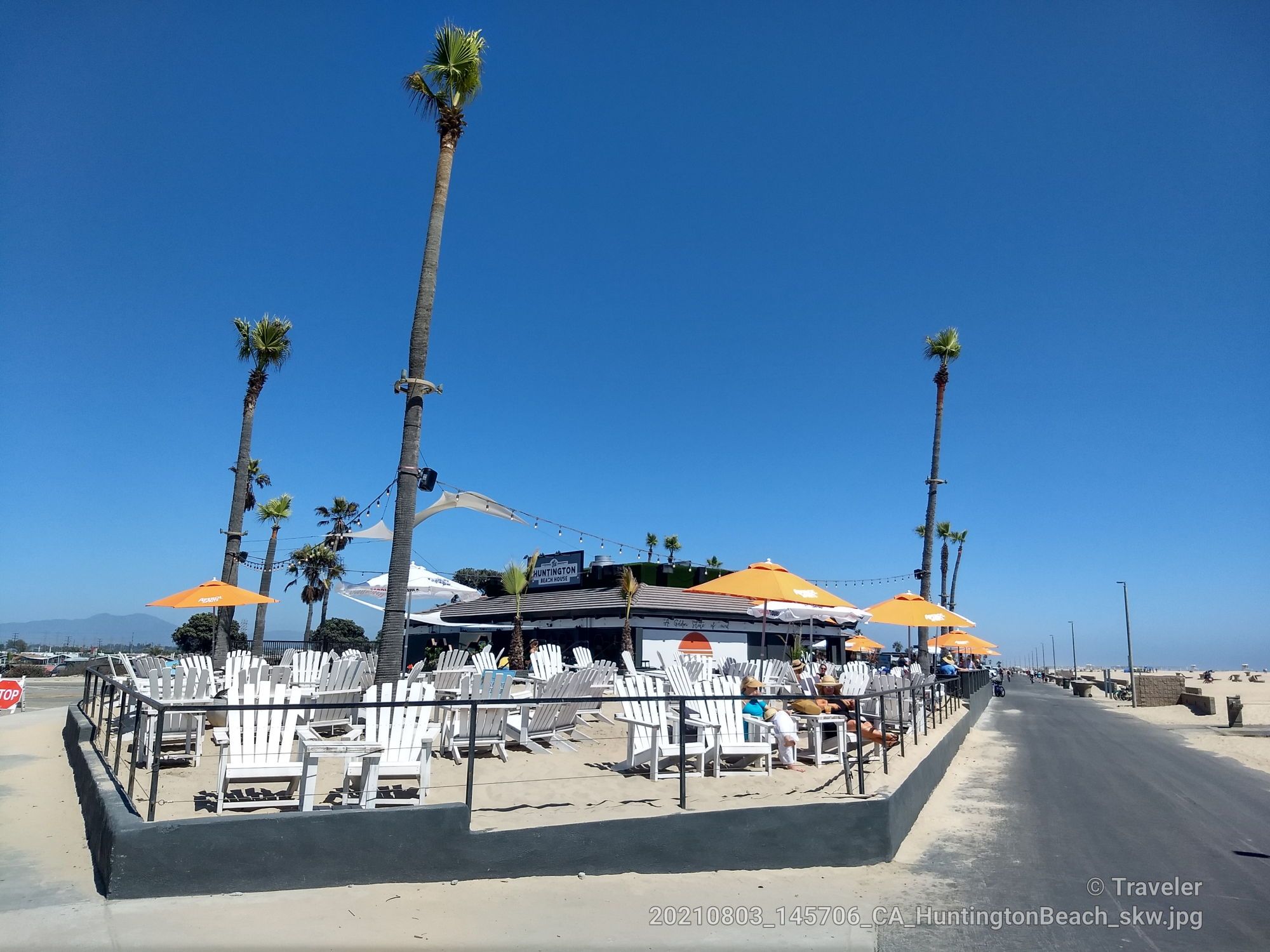 Outdoor cafe with white chairs, orange umbrellas, and tall palm trees. - Huntington City Beach – Huntington Beach Pier loop from Huntington State Beach