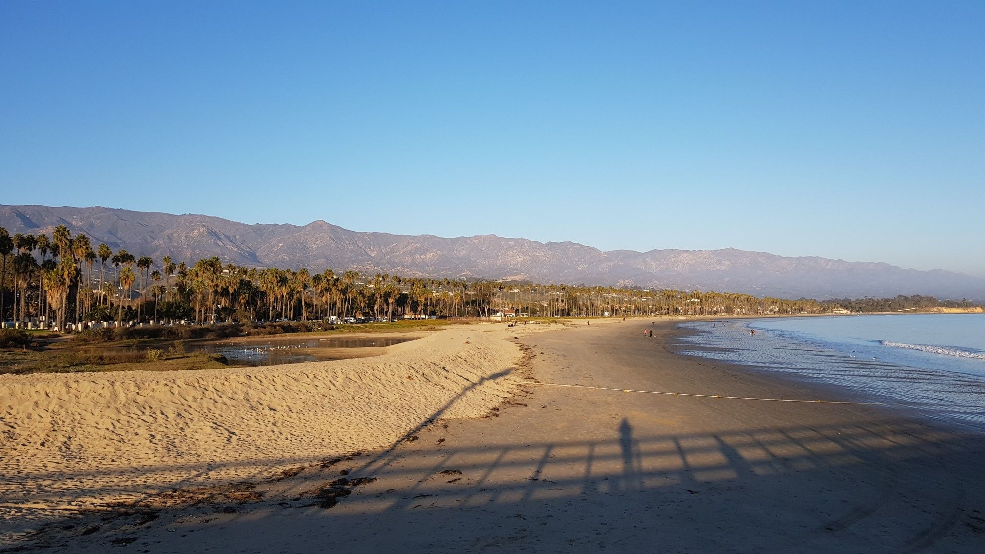 Expansive sandy beach, calm ocean, palm trees, and distant mountains at sunset. - Santa Barbara Stearns Wharf