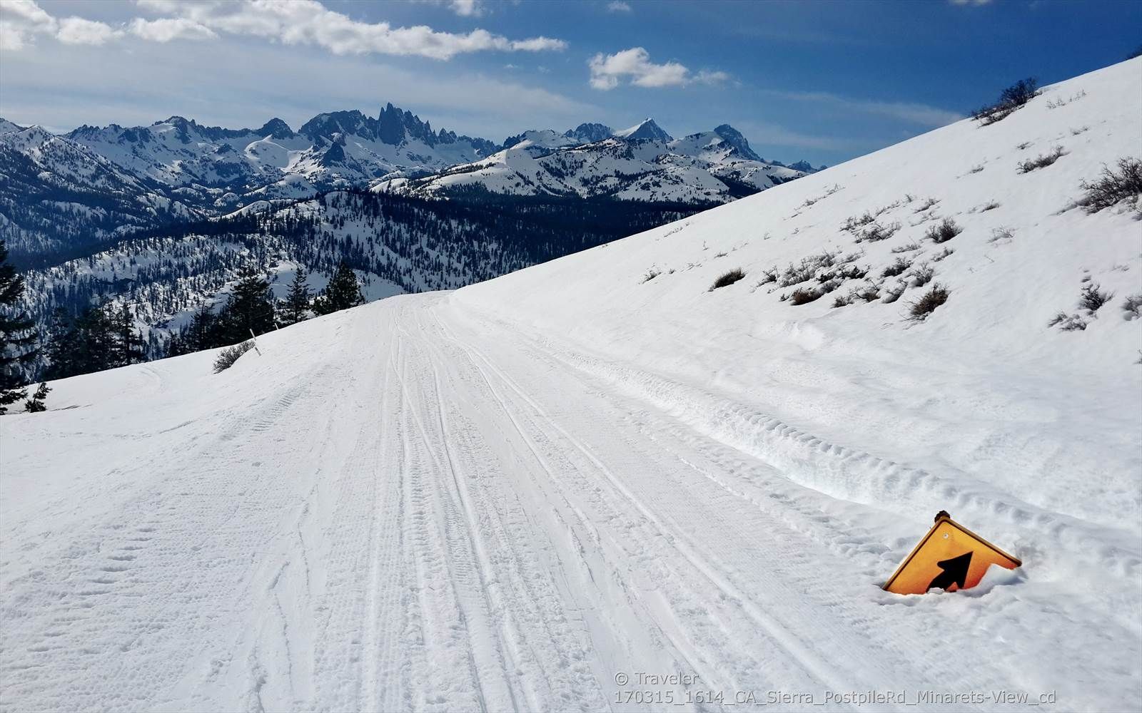 A wide snowy slope with an orange marker and distant jagged mountains. - Starkweather Lake Trail