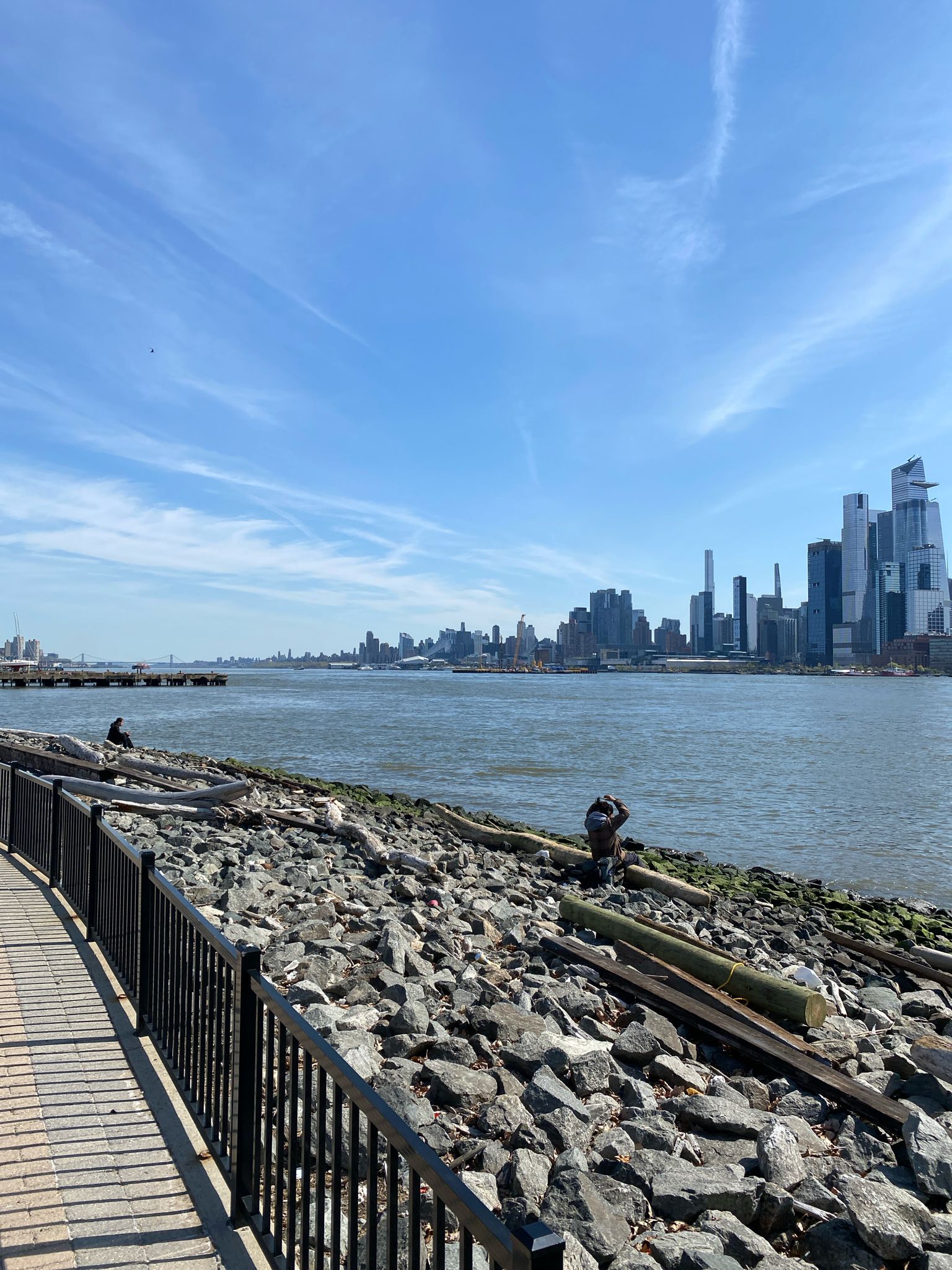 Waterfront path alongside a rocky shore with a distant city under a blue sky. - Weehawken Cove loop from Hoboken