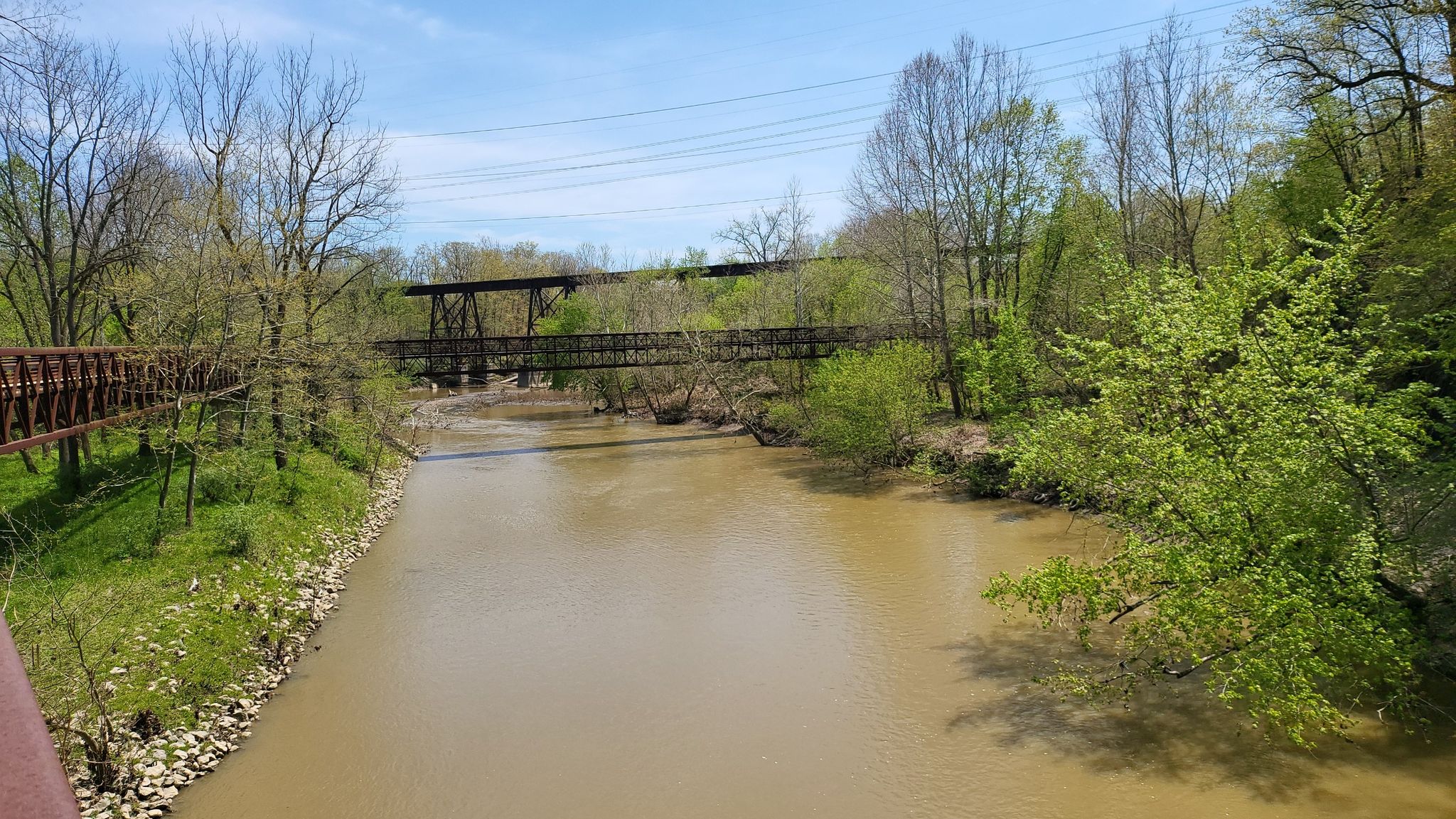 Muddy river flowing under two bridges, surrounded by trees with new leaves. - Black River – Black River Bridge loop from Century Park