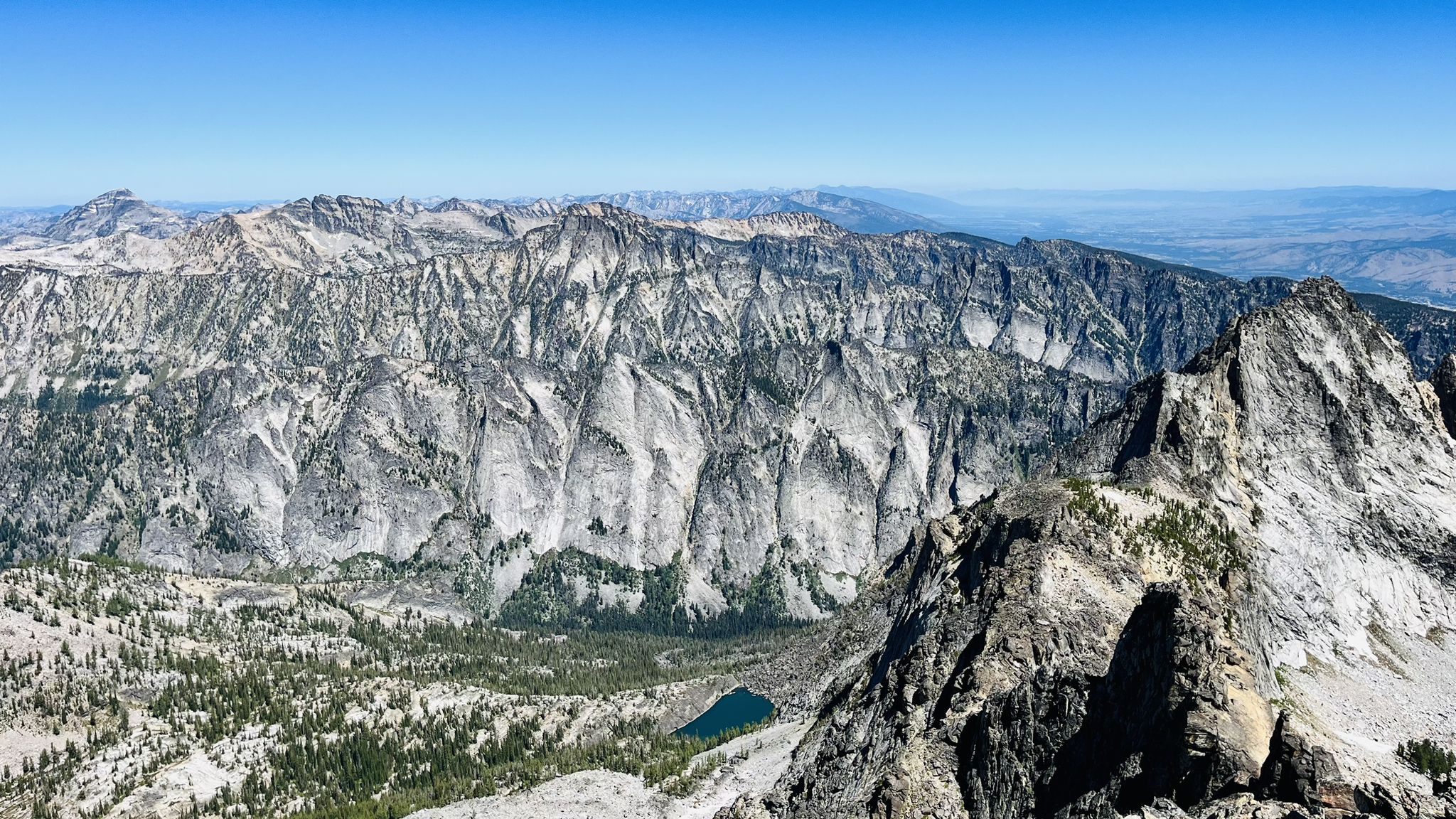 Panoramic view of rugged mountains, a small lake, and clear blue sky. - Trapper Peak Trail