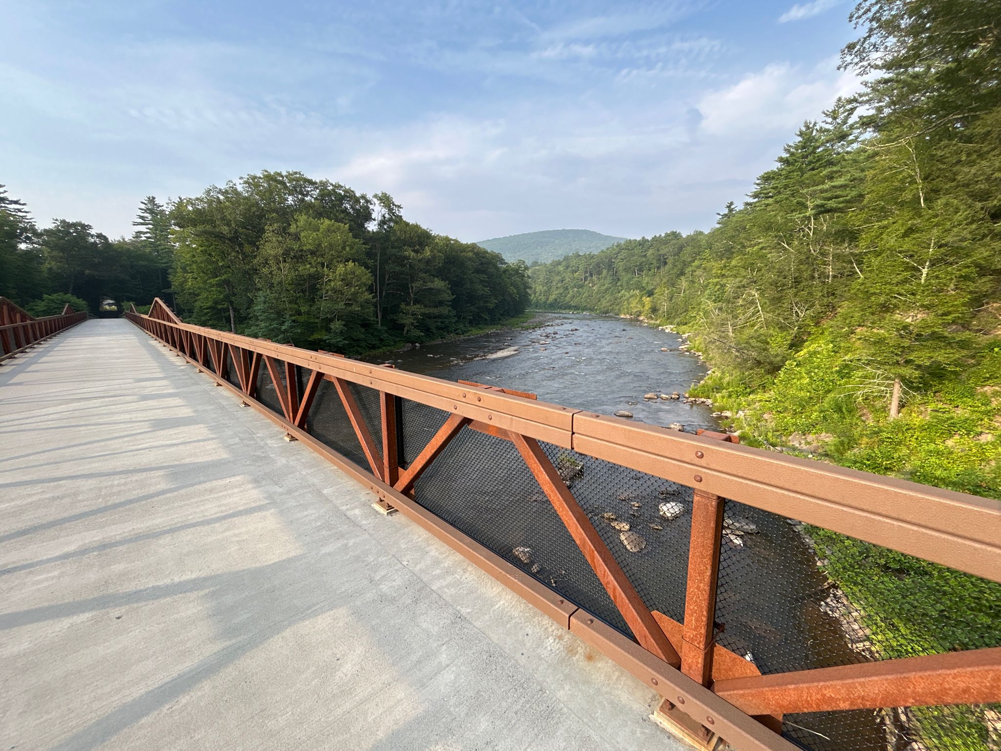 Long pedestrian bridge over a river, surrounded by green forest and hills. - Frozen Ashokan Reservoir loop from Shokan