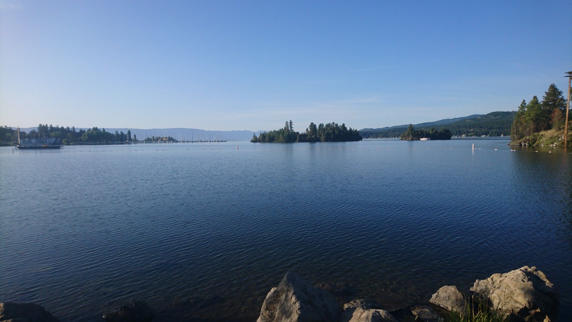 Wide view of a calm lake with forested islands under a clear sky. - Great Northern Historical Trail
