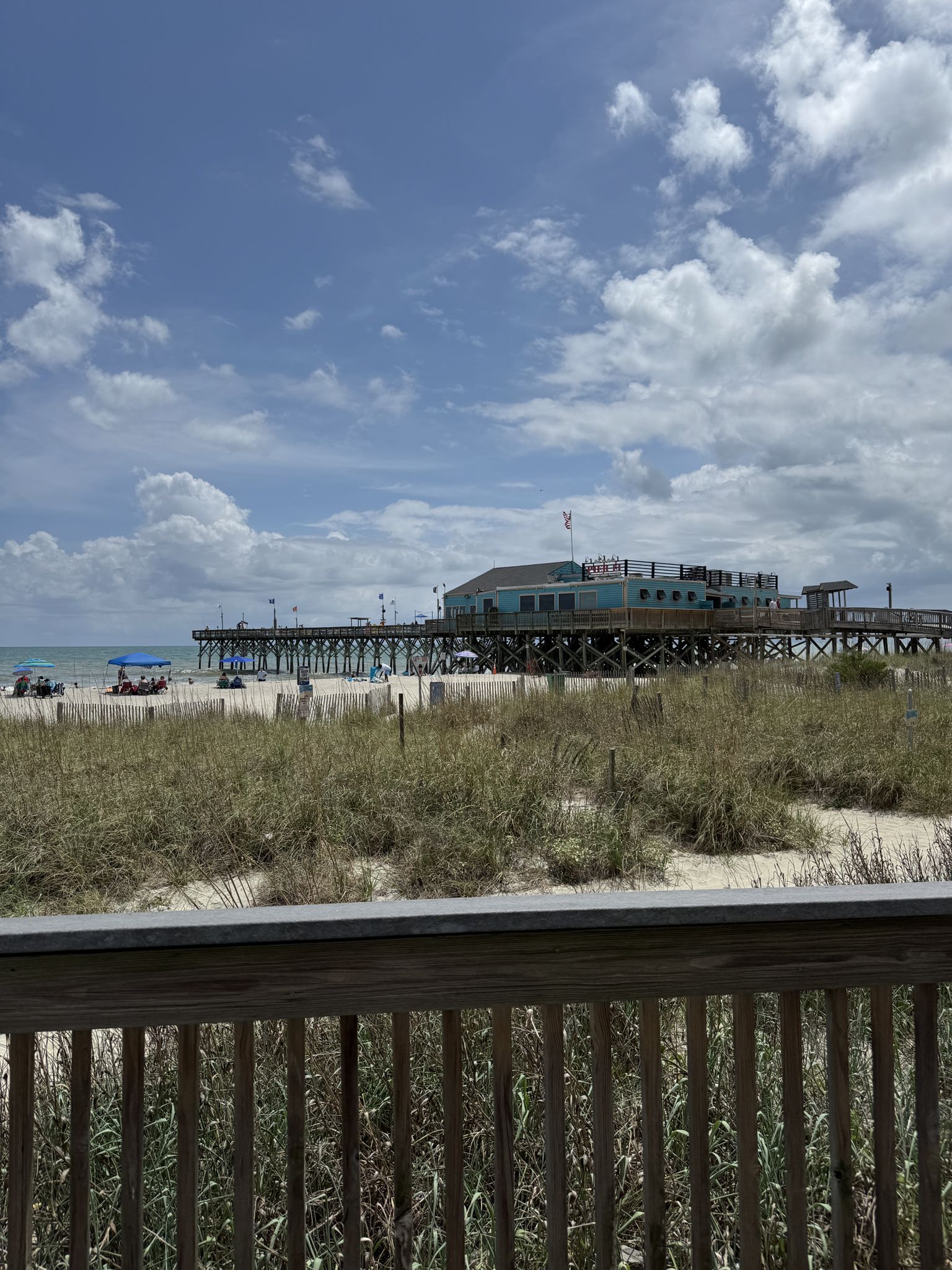 Long pier over ocean with beach, tall grass, and cloudy sky. - Myrtle Beach State Park to Boardwalk Beach Walk