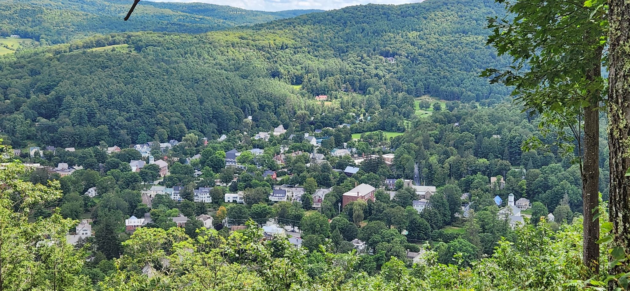 Overlook of a small town nestled within dense green forested hills. - Running loop from Woodstock