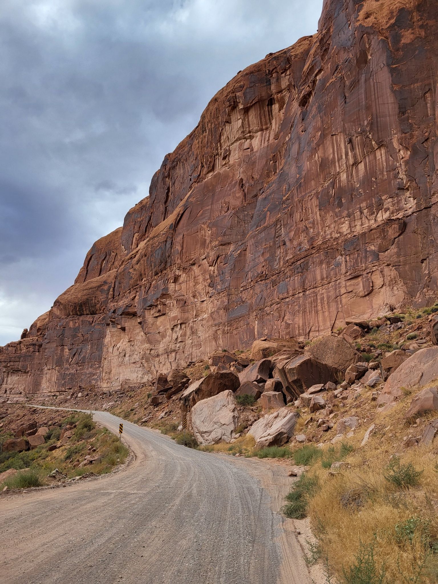 Mountain biker on a dirt road at the base of a massive red rock cliff. - Hurrah Pass