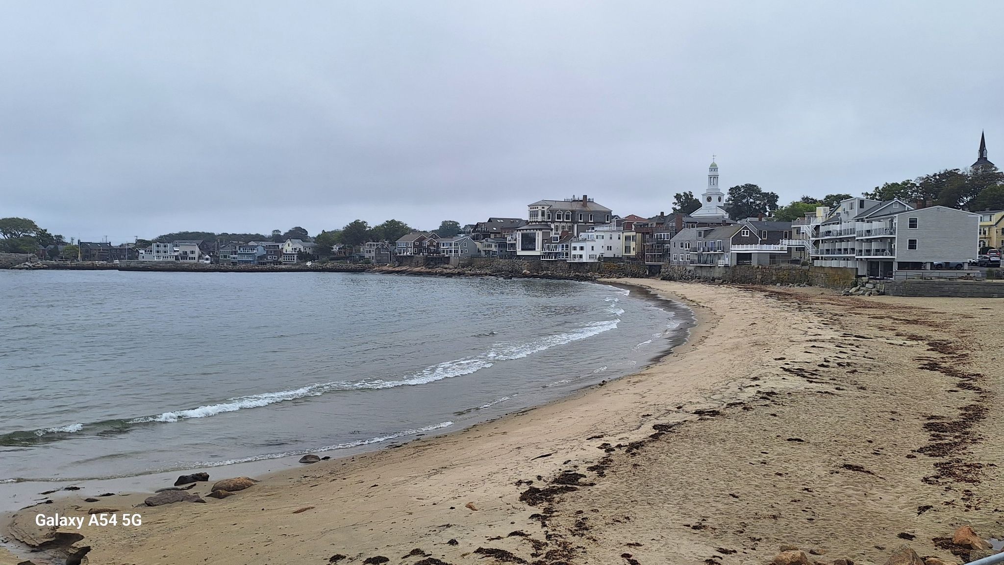 Sandy beach with gentle waves and a coastal town under an overcast sky. - Good Harbor Beach – Old Garden Beach loop from Rockport