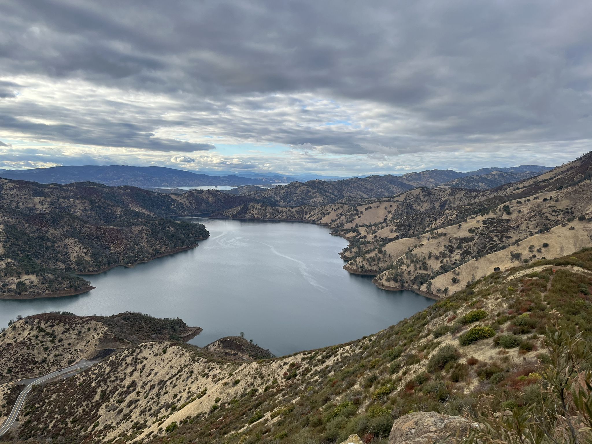 Wide view of a lake winding through dry, rugged mountains under a cloudy sky. - Blue Ridge and Homestead Loop