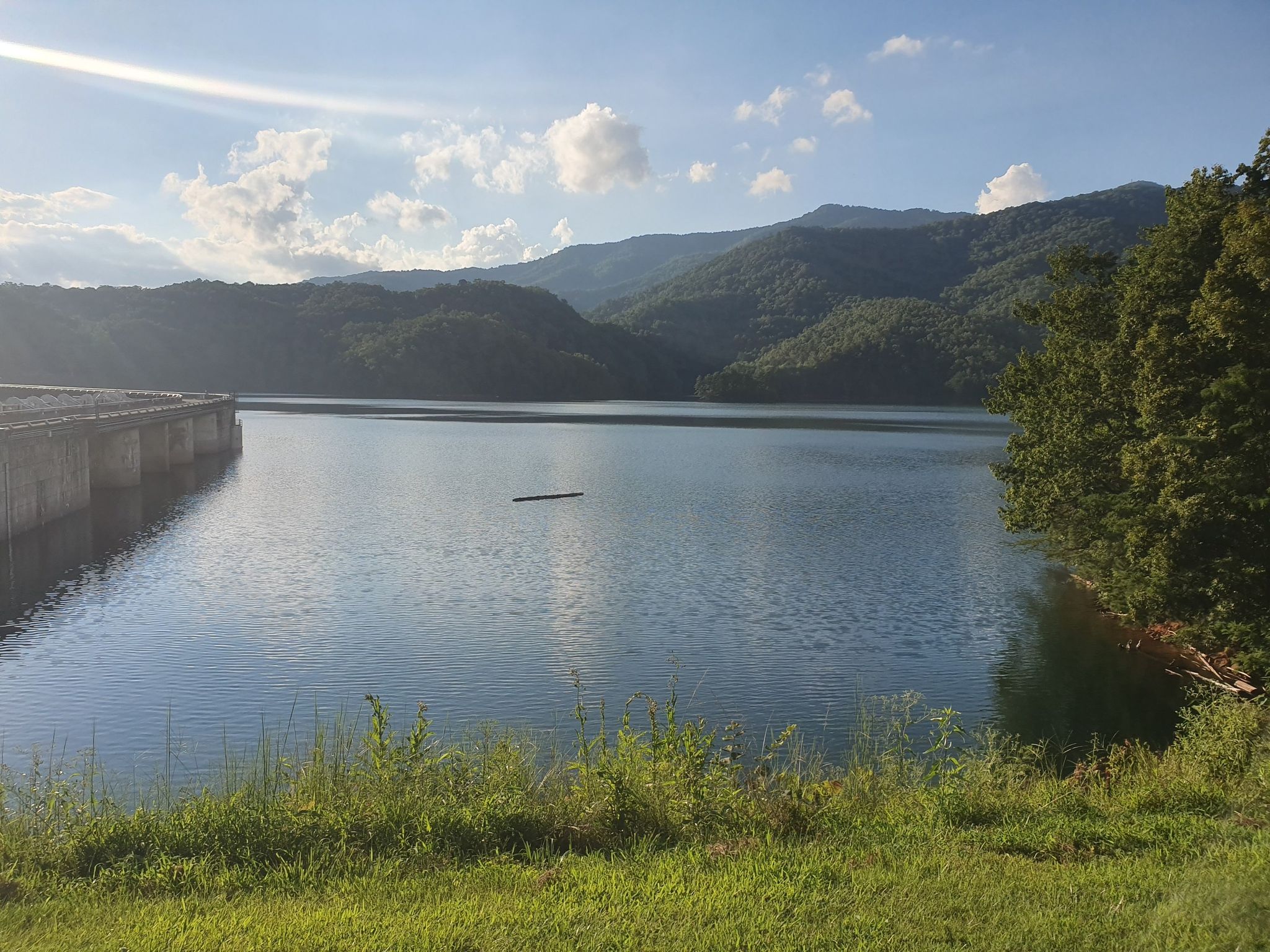 A wide lake with a concrete dam, forested mountains, and a bright sunny sky. - Shuckstack Fire Tower via Appalachian Trail