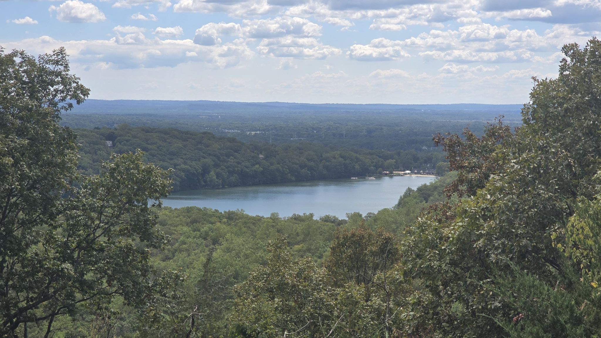 Overhead view of a lake surrounded by green forests under a cloudy sky. - Lake Valhalla Overlook via Yellow, Orange, and Green Dot Trails