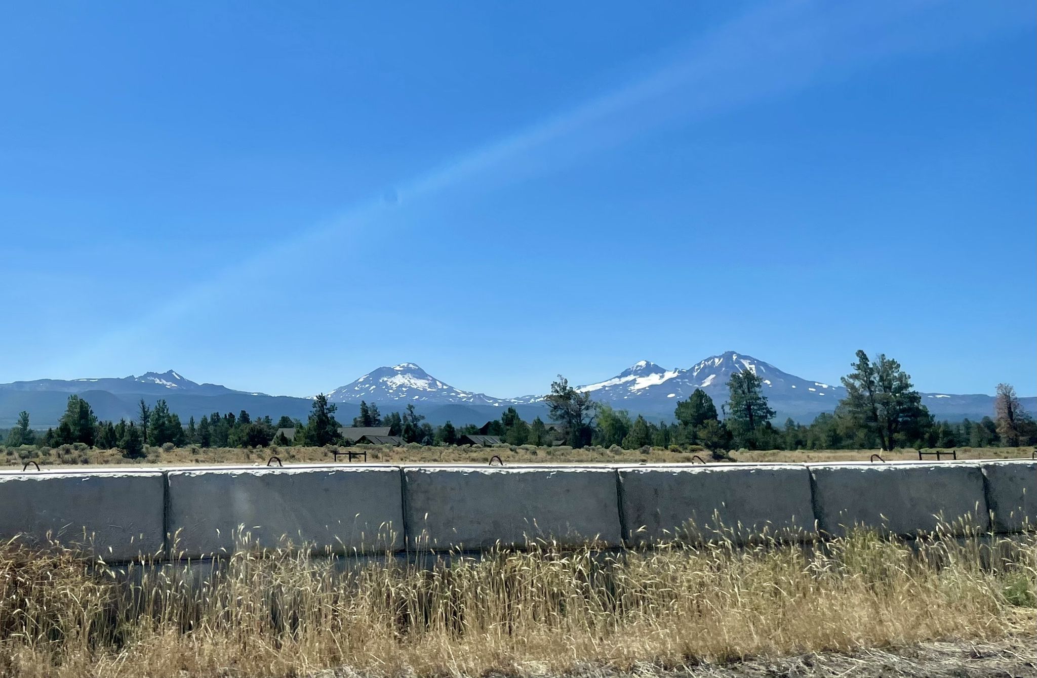 Distant snow-capped mountains under a clear blue sky, seen from a roadside. - Sisters and Twin Bridges Scenic Bikeway Loop