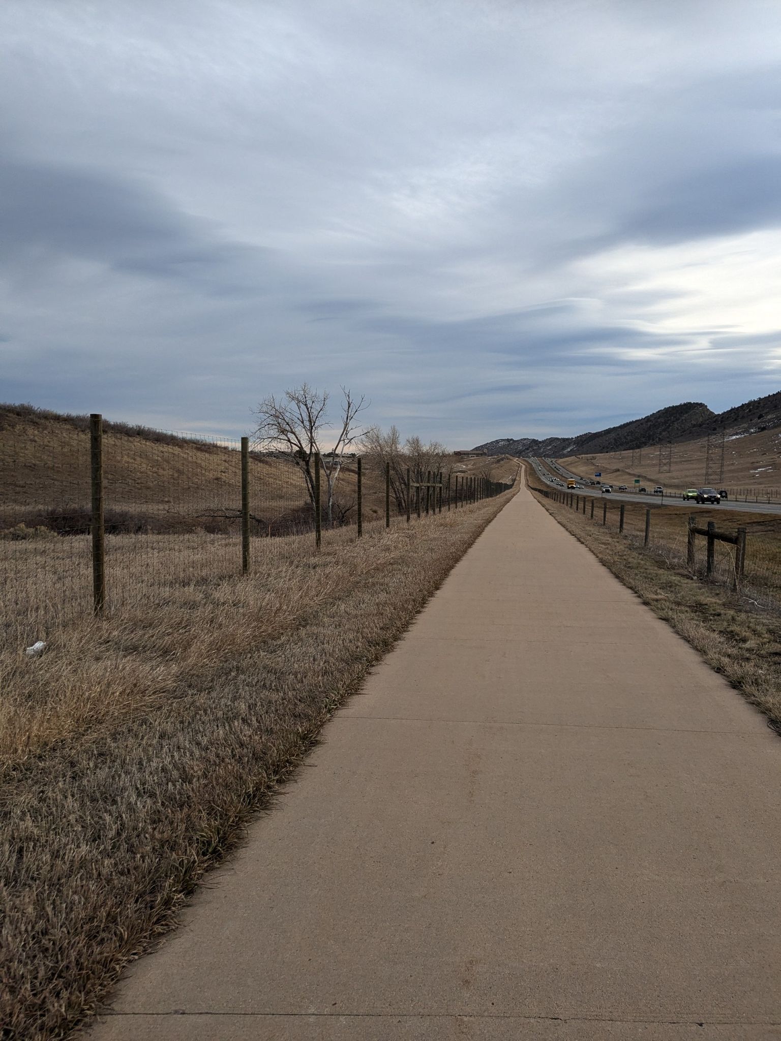 Long paved path next to a fence and dry hills under an overcast sky. - Mann Reservoir – Pleasant Park Grange Rest Stop loop from Dakota Ridge High School
