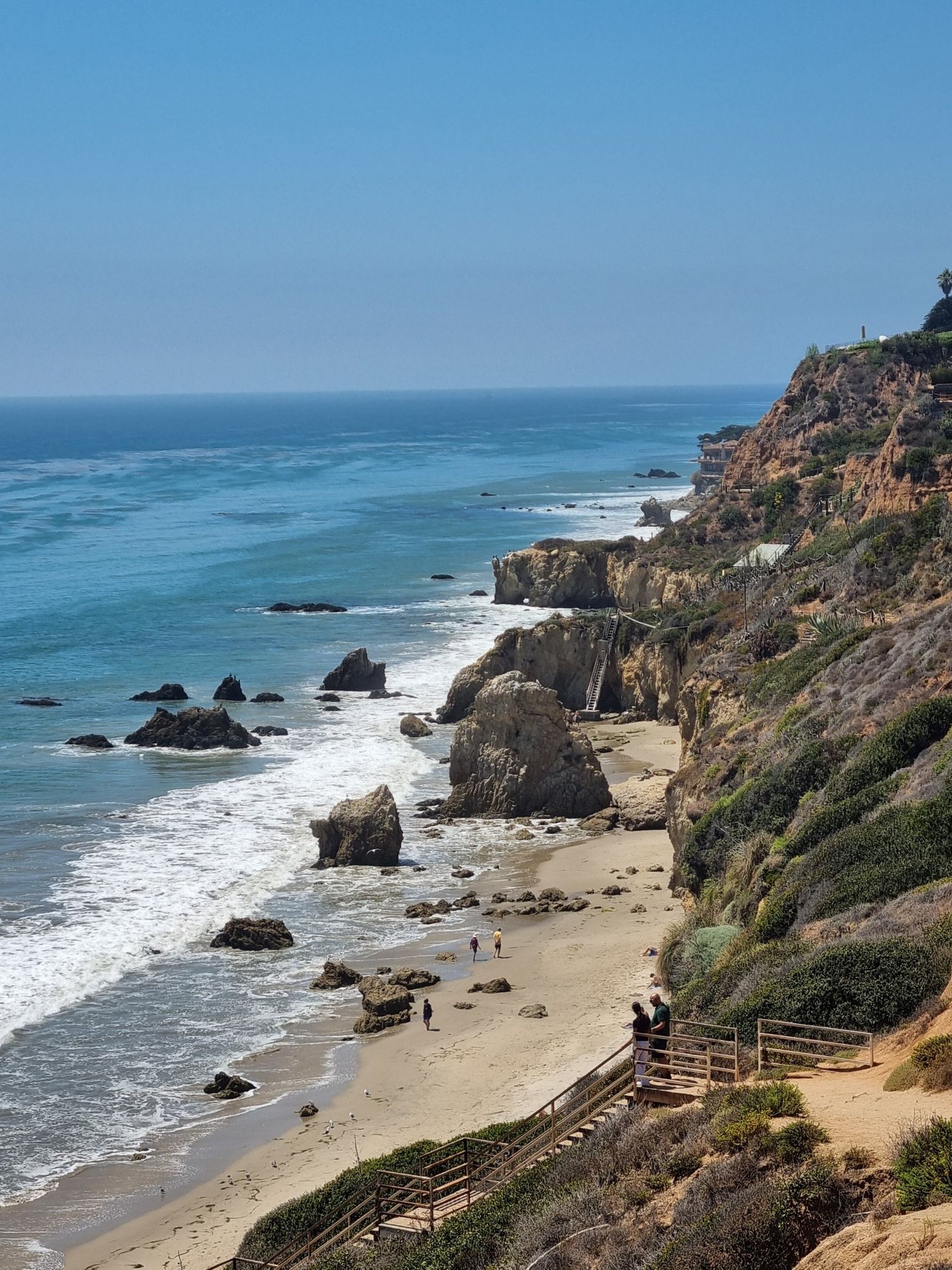 Overhead view of a sunny beach, ocean, rocky coastline, and people on stairs. - El Matador, La Piedra and El Pescador State Beaches