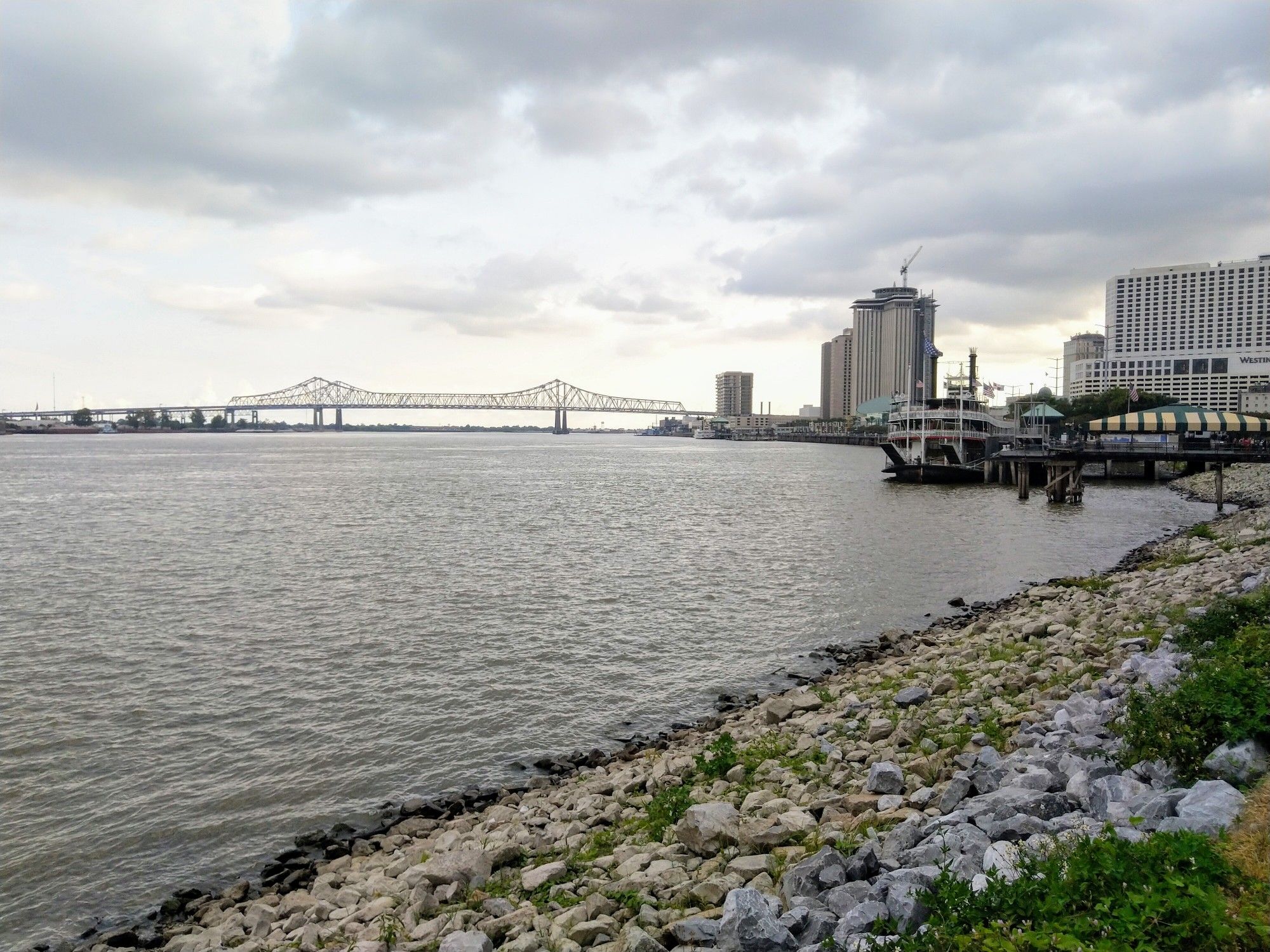 Wide river with a distant bridge and city skyline under cloudy skies. - Steamboat Natchez – Big Lake City Park loop from New Orleans