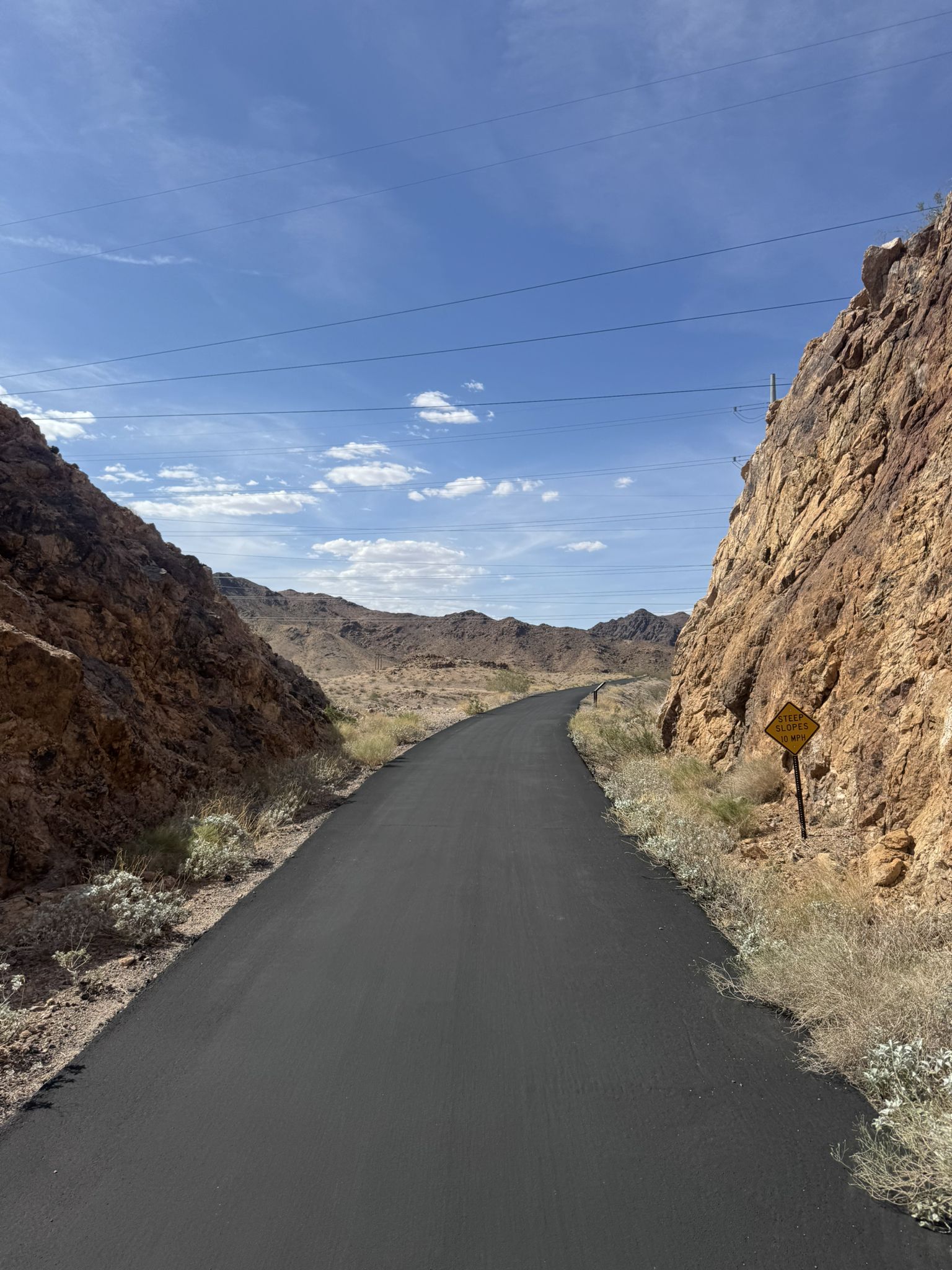 Paved road winds through a narrow rocky canyon under a blue sky. - Boulder Dam Hotel – Boulder Theatre loop from Boulder Beach South
