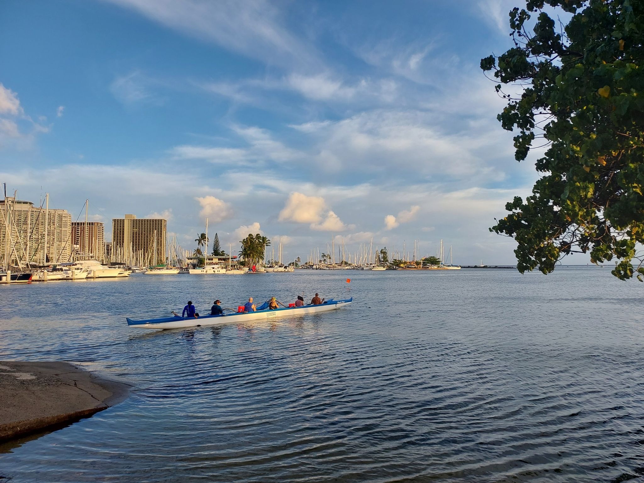 People paddling an outrigger canoe on calm water, city skyline, sunny. - Honolulu to Sand Island loop
