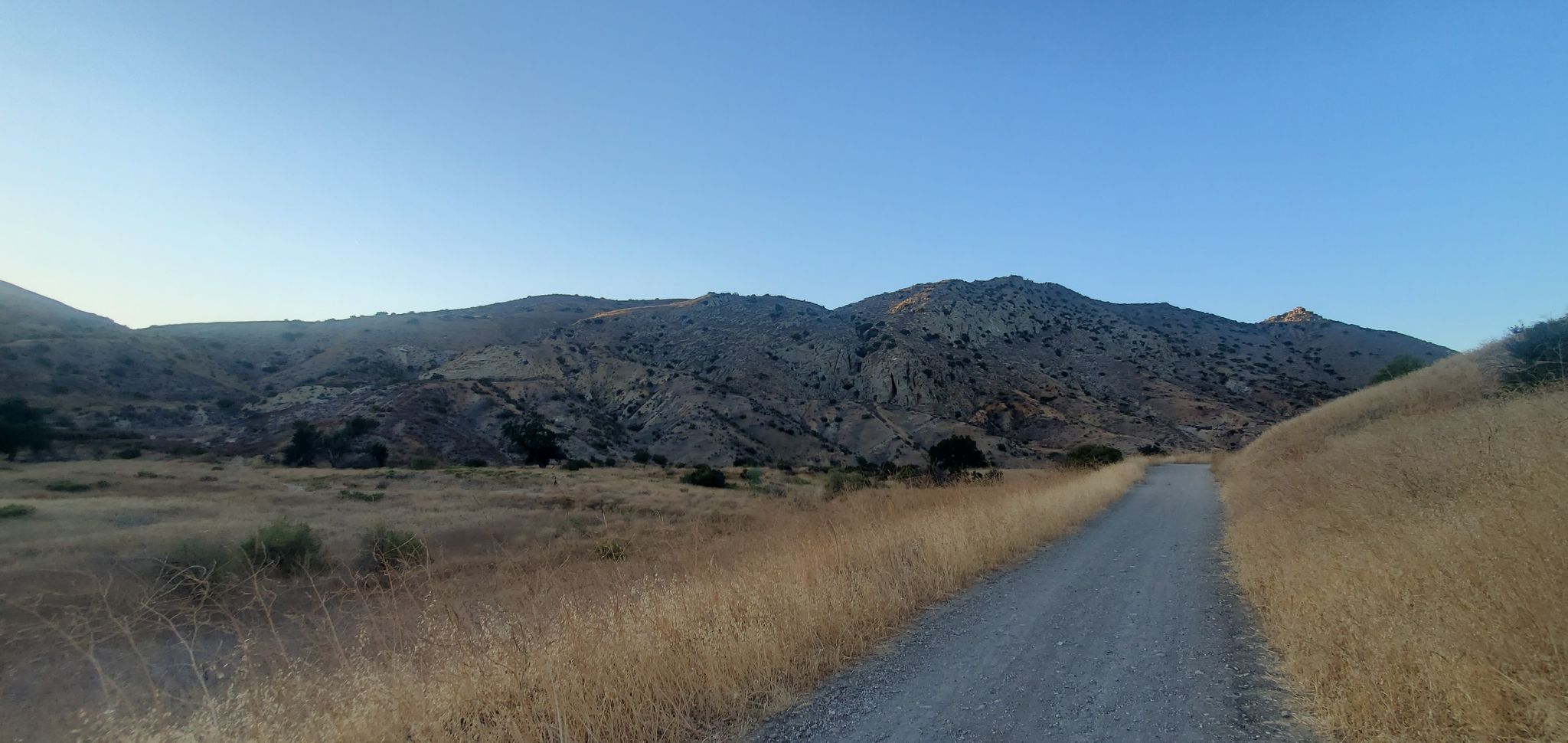 Dirt road through dry grass fields with rugged mountains under a clear sky. - Victory Trailhead – El Escorpion Park loop from El Escorpion Park