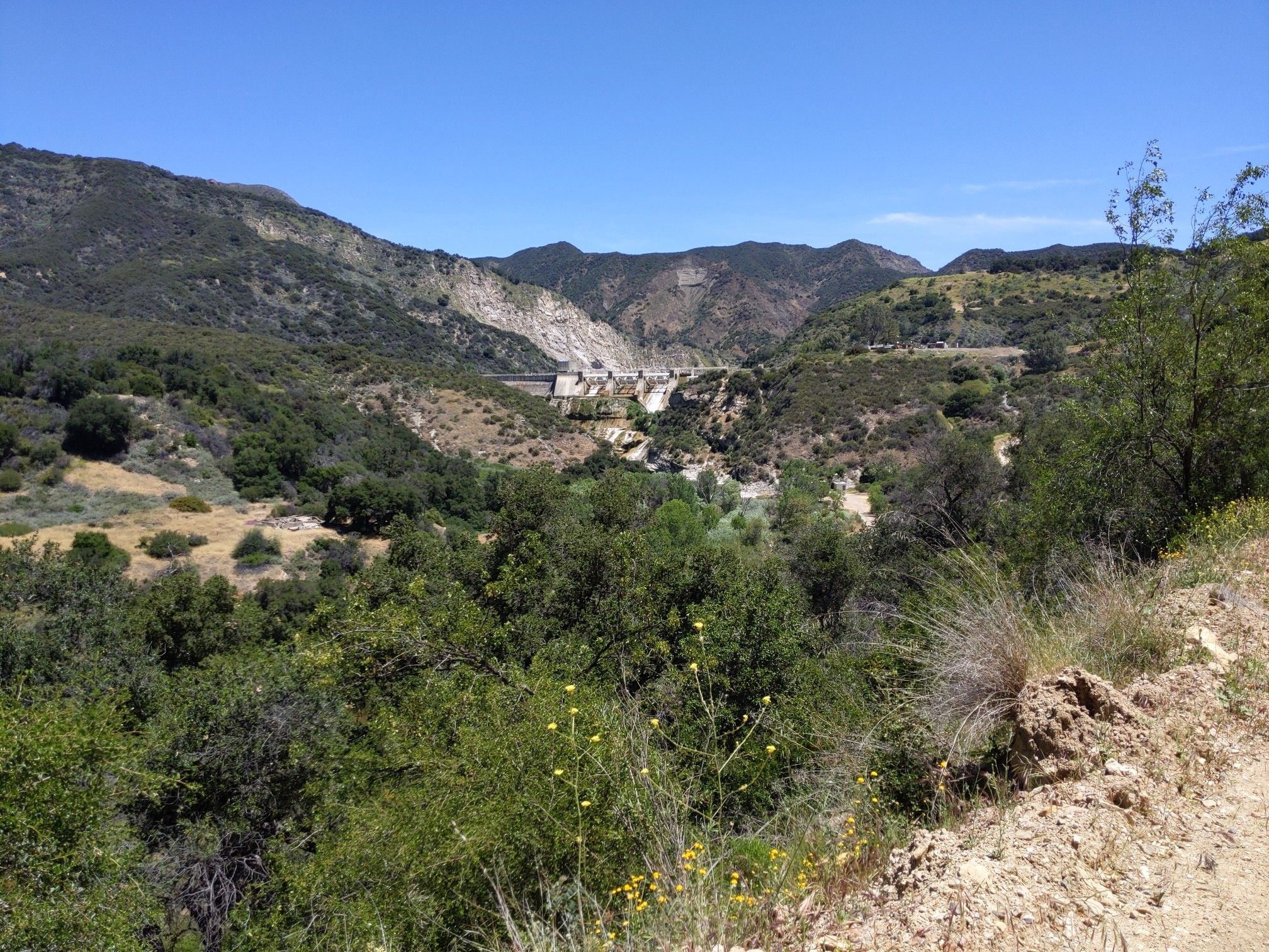 Sunny valley with green trees, distant mountains, and a large concrete structure. - Red Rock Trail Loop