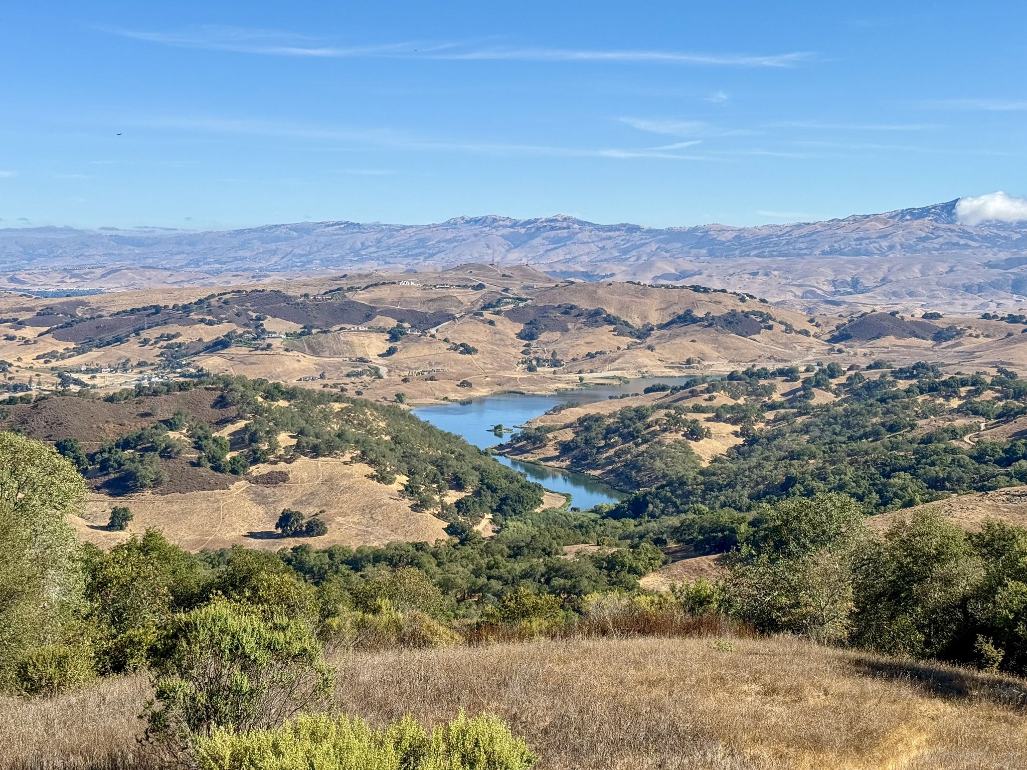 Panoramic view of a lake nestled among dry, rolling hills and distant mountains. - Rancho Canada del Oro and Calero Park Loop