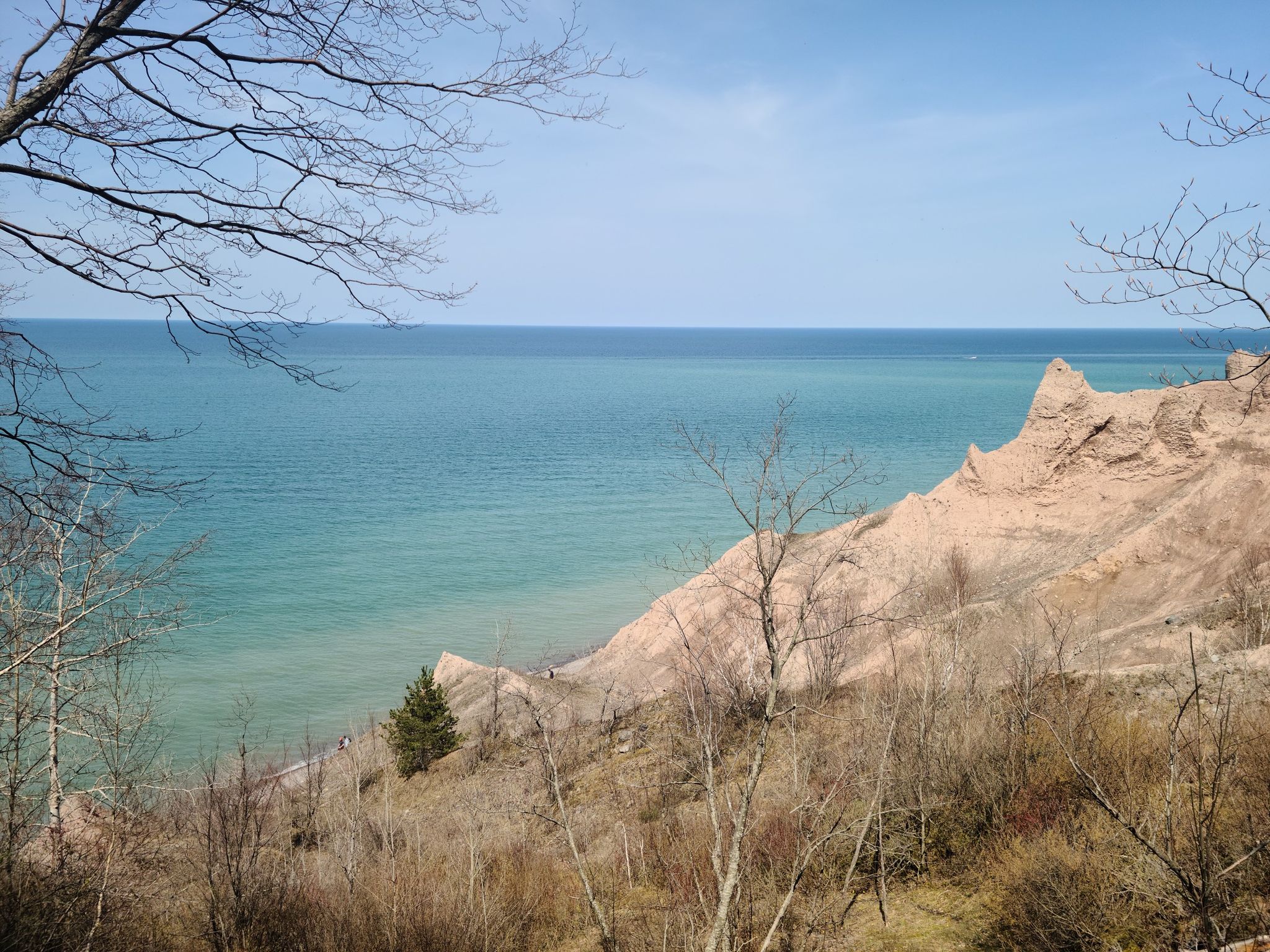 Bare trees frame eroded cliffs and a wide blue sea on a sunny day. - Chimney Bluffs – Chimney Bluffs loop from Chimney Bluffs State Park