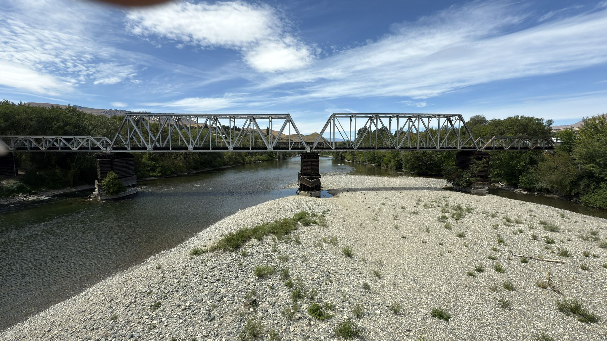 Metal truss bridge over a river, rocky shore, green trees, sunny day. - Wenatchee Confluence Trail