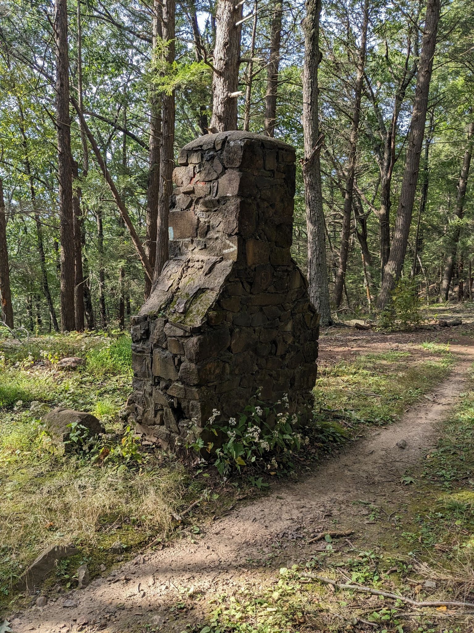 An old stone chimney stands beside a dirt path in a sun-dappled forest. - Hatchett Hill loop from Tariffville